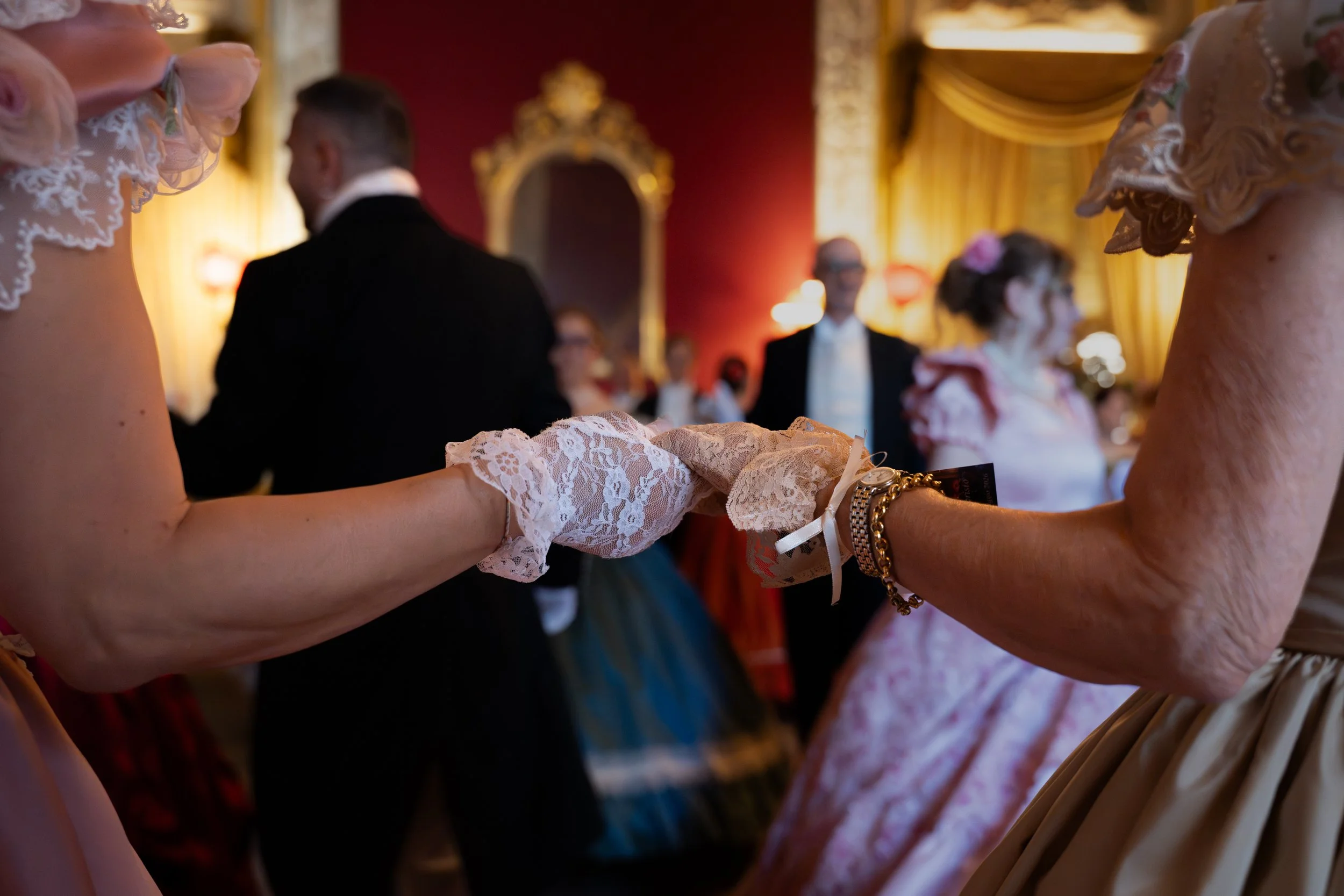 Persone che ballano un ballo tradizionale in un ambiente elegante, con tende dorate e un grande specchio dorato sul muro di sfondo.