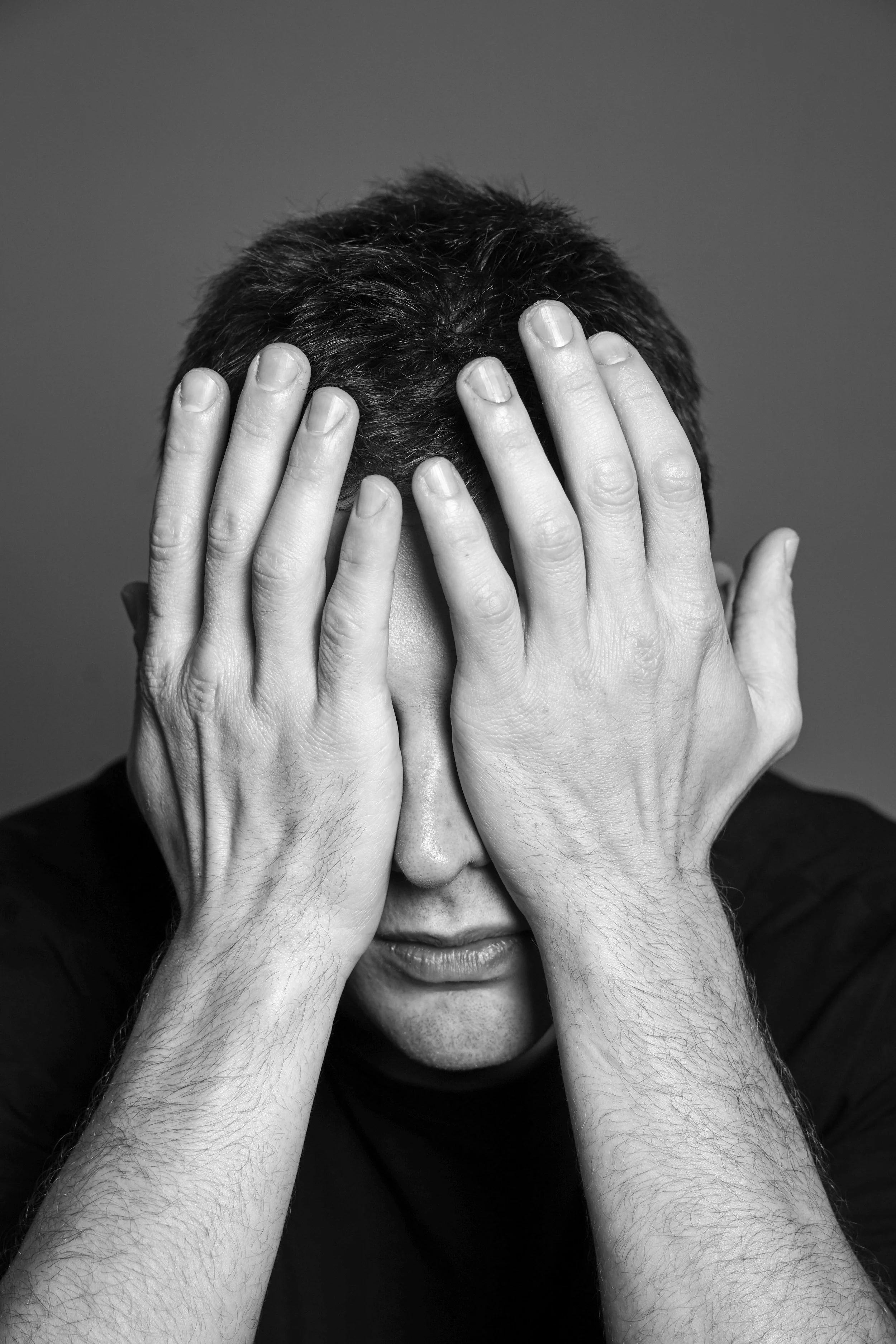 Uomo con capelli scuri coprendosi gli occhi con le mani