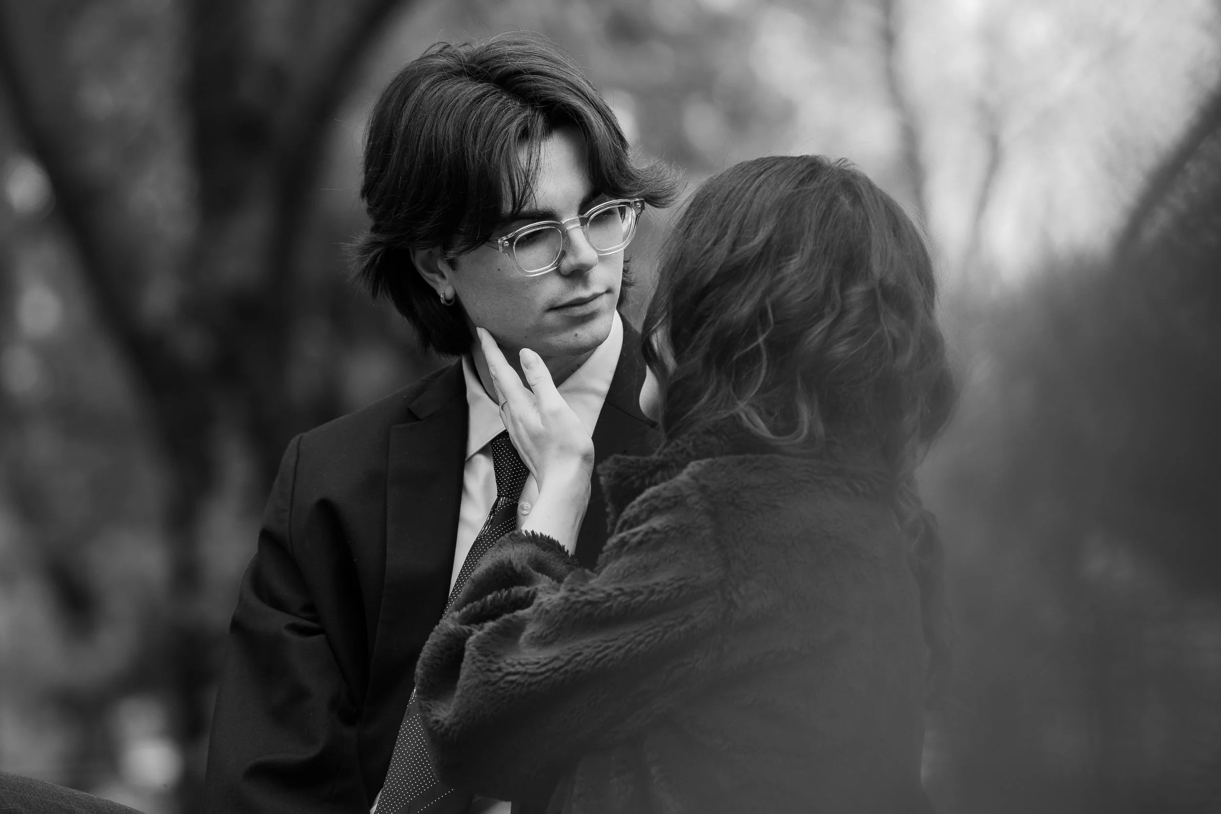 Due persone, una donna e un uomo, si guardano intensamente, con la donna che tocca delicatamente il viso dell'uomo. Sfondo naturale sfocato, in bianco e nero.