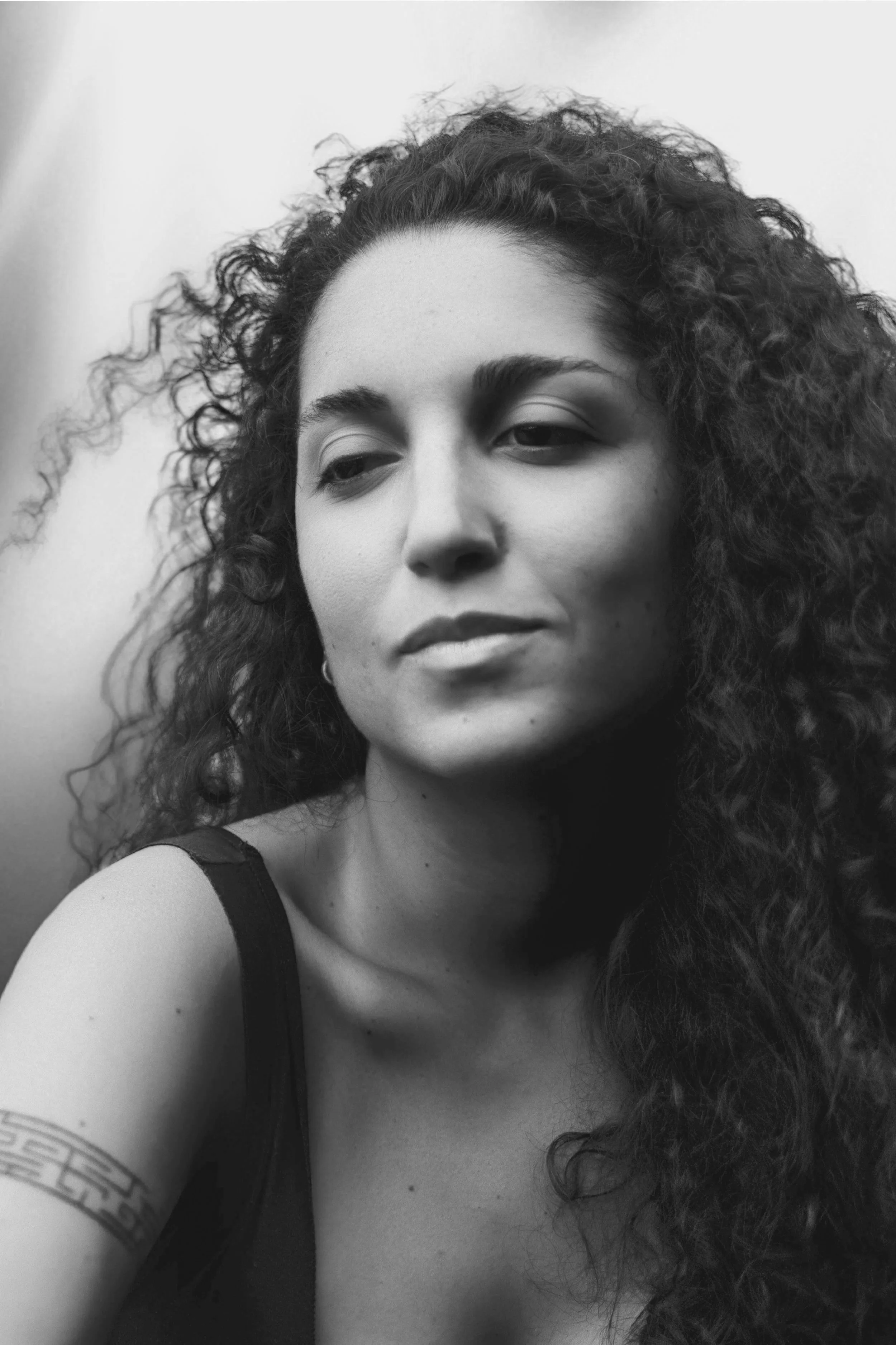 Ritratto in bianco e nero di una donna con capelli ricci che guarda leggermente di lato, mentre indossa una maglietta a spalle strette.