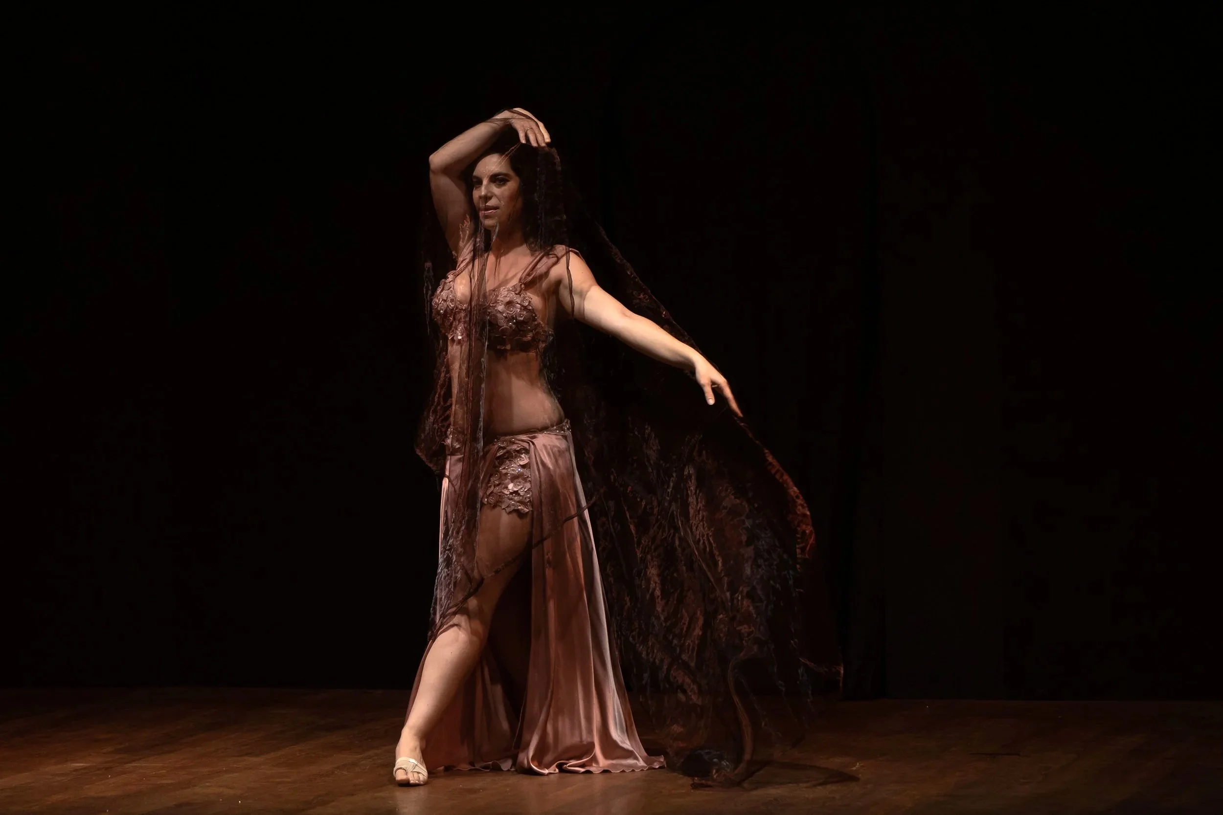 Donna in abito da sera rosa con lungo velo nero che danza sul palco con sfondo nero.