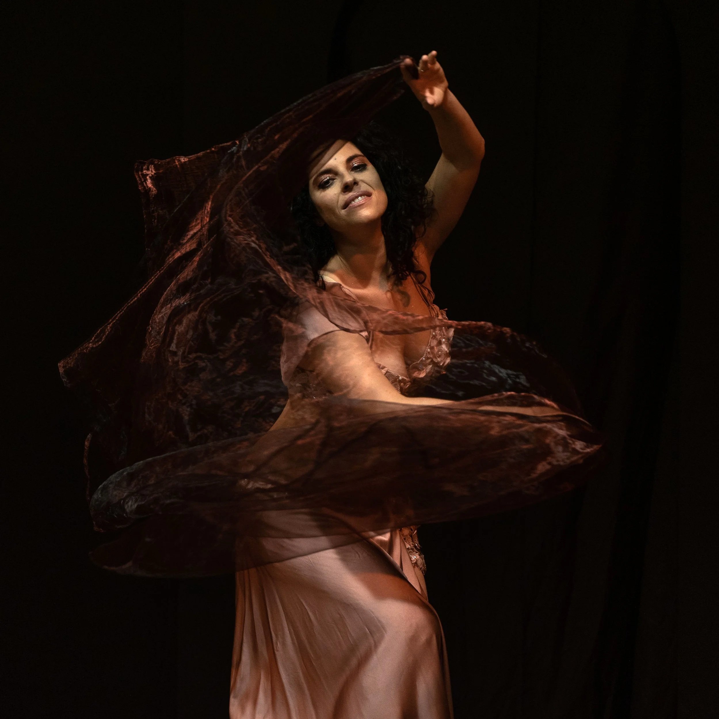 Donna che danza con un abito di tessuto leggero, nel buio, con cappello di tessuto trasparente che si muove al suo ritmo.