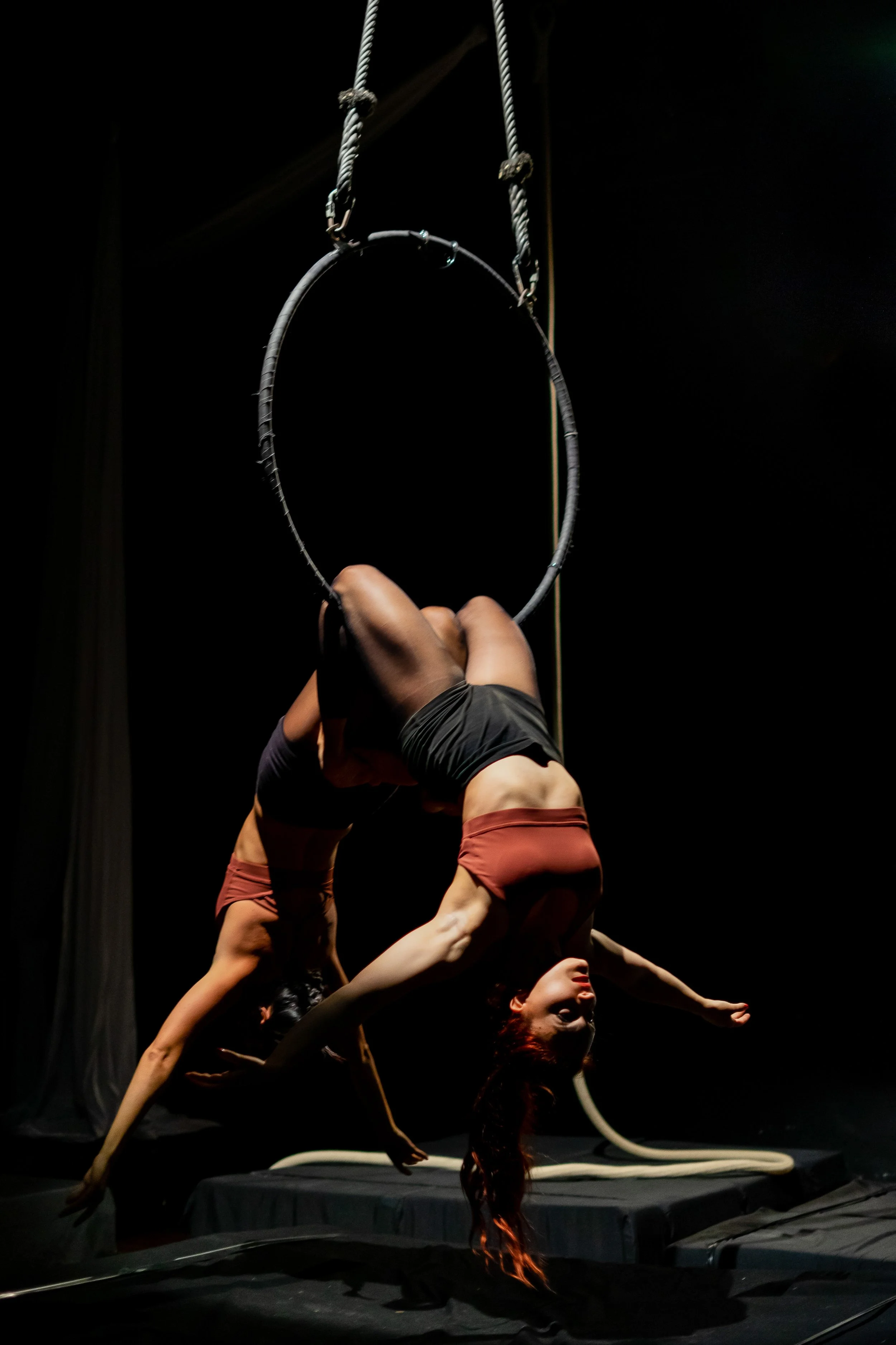 Due acrobati si esibiscono in uno spettacolo teatrale, uno di loro si trova in posizione capovolta mentre l'altro la sostiene, con un cerchio sospeso sopra di loro.