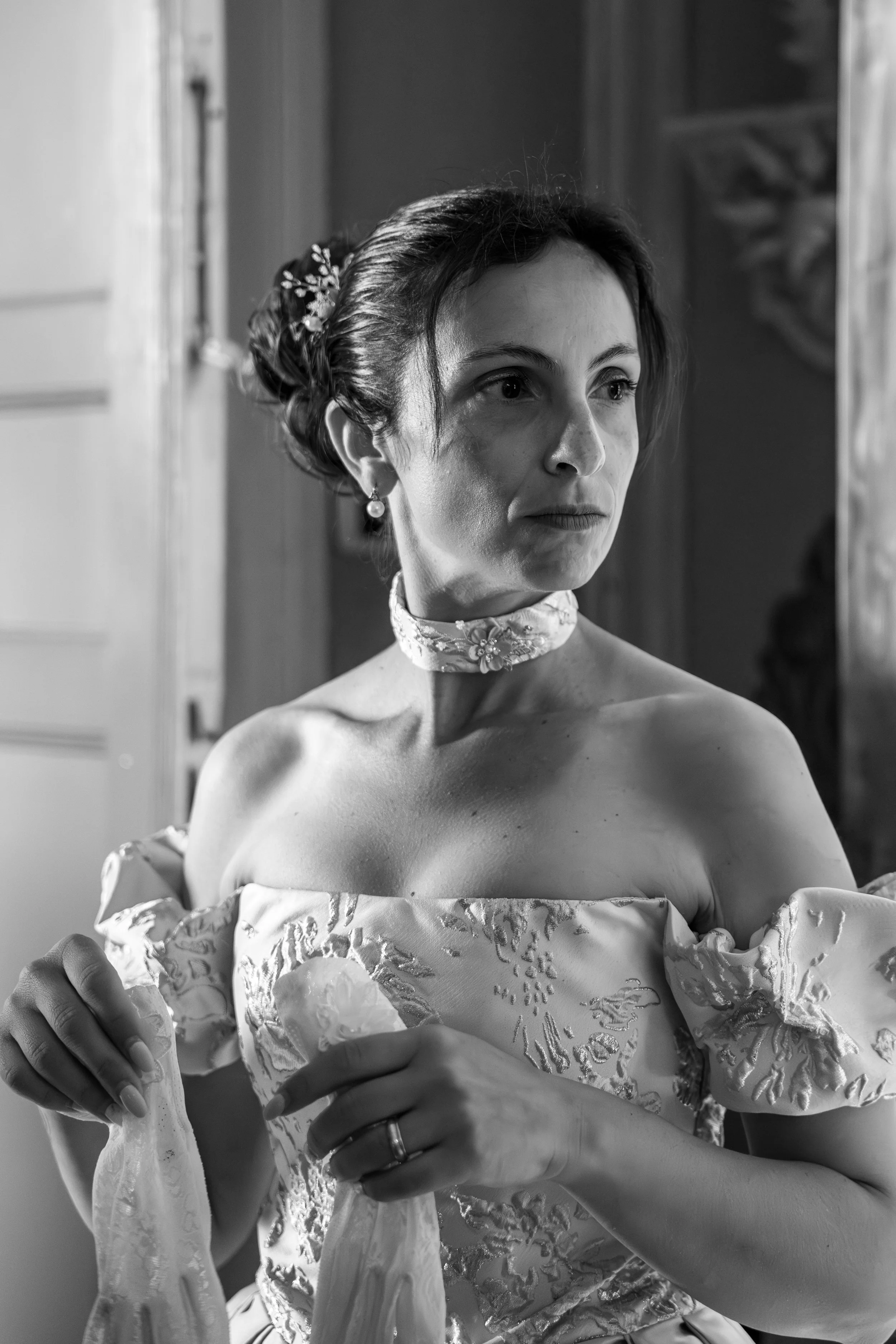 Ritratto di una donna in abito elegante con riccioli e orecchini, che si sta sistemando un abito.