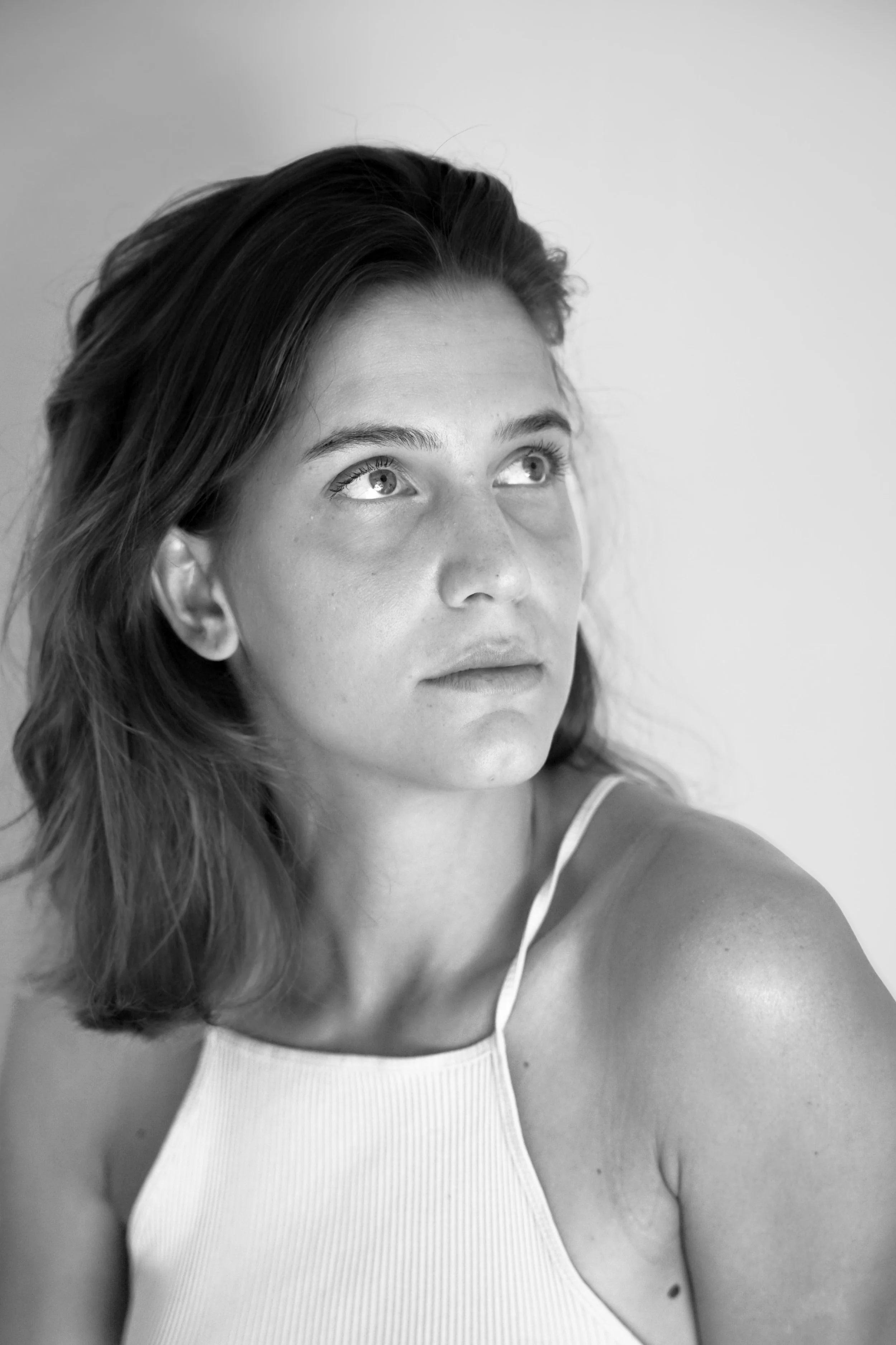 Ritratto in bianco e nero di una giovane donna con capelli castani, occhi chiari, che guarda verso l'alto, con spalle nude e maglietta bianca.