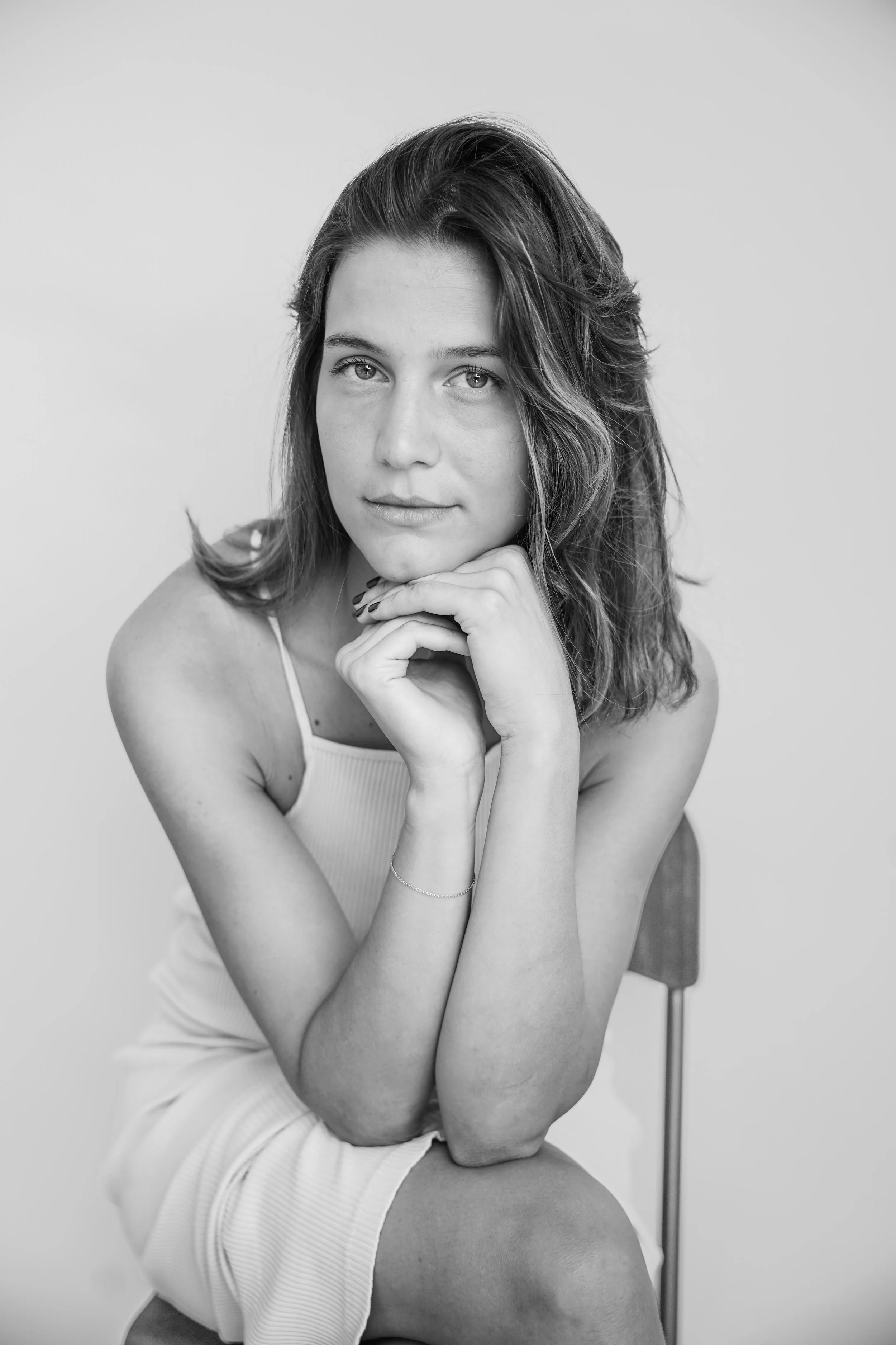 Ritratto in bianco e nero di una giovane donna seduta su una sedia, con mano sotto il mento, che guarda verso l'obiettivo.