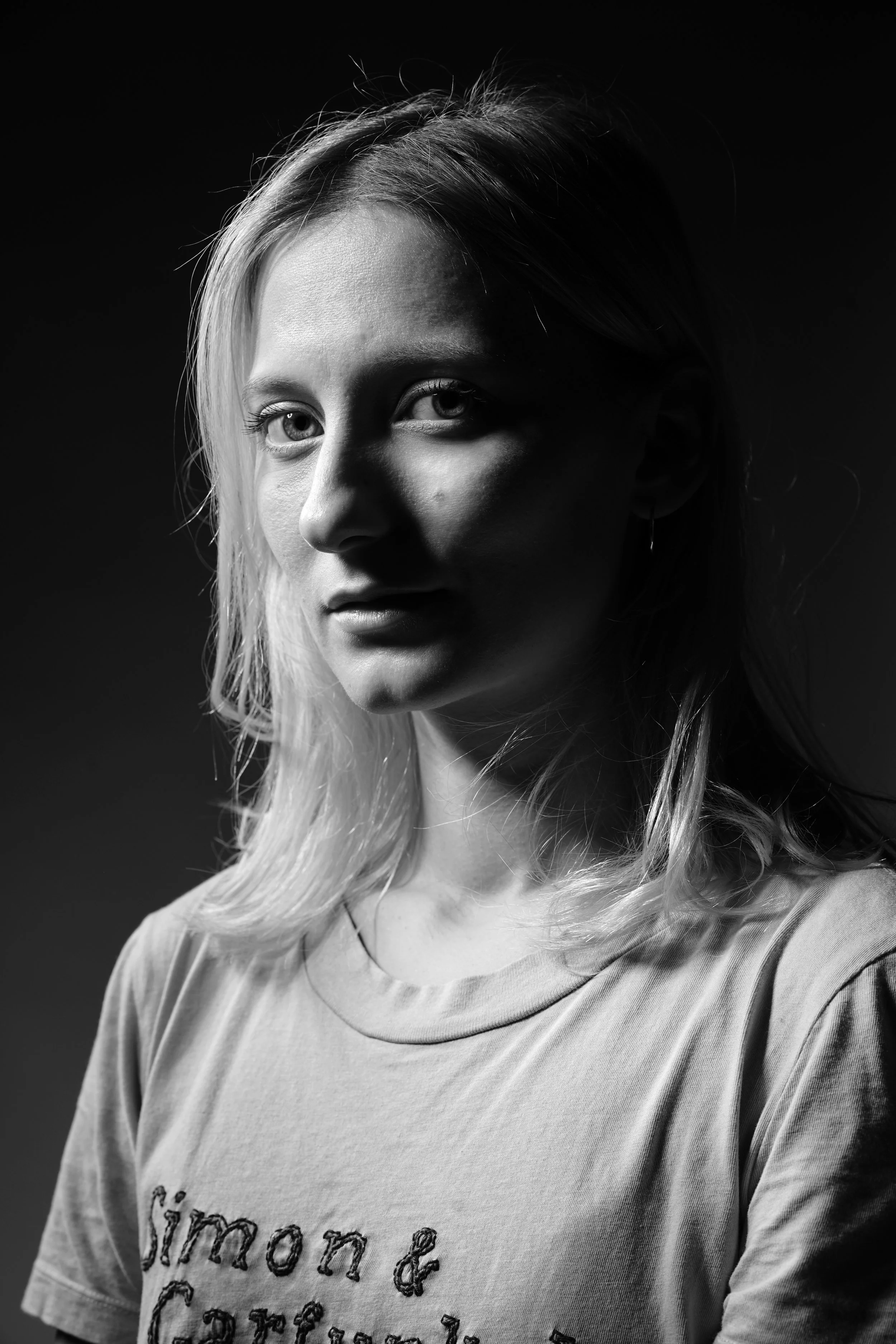 Ragazza con capelli biondi, maglietta con scritte, illuminata lateralmente in uno stile in bianco e nero.