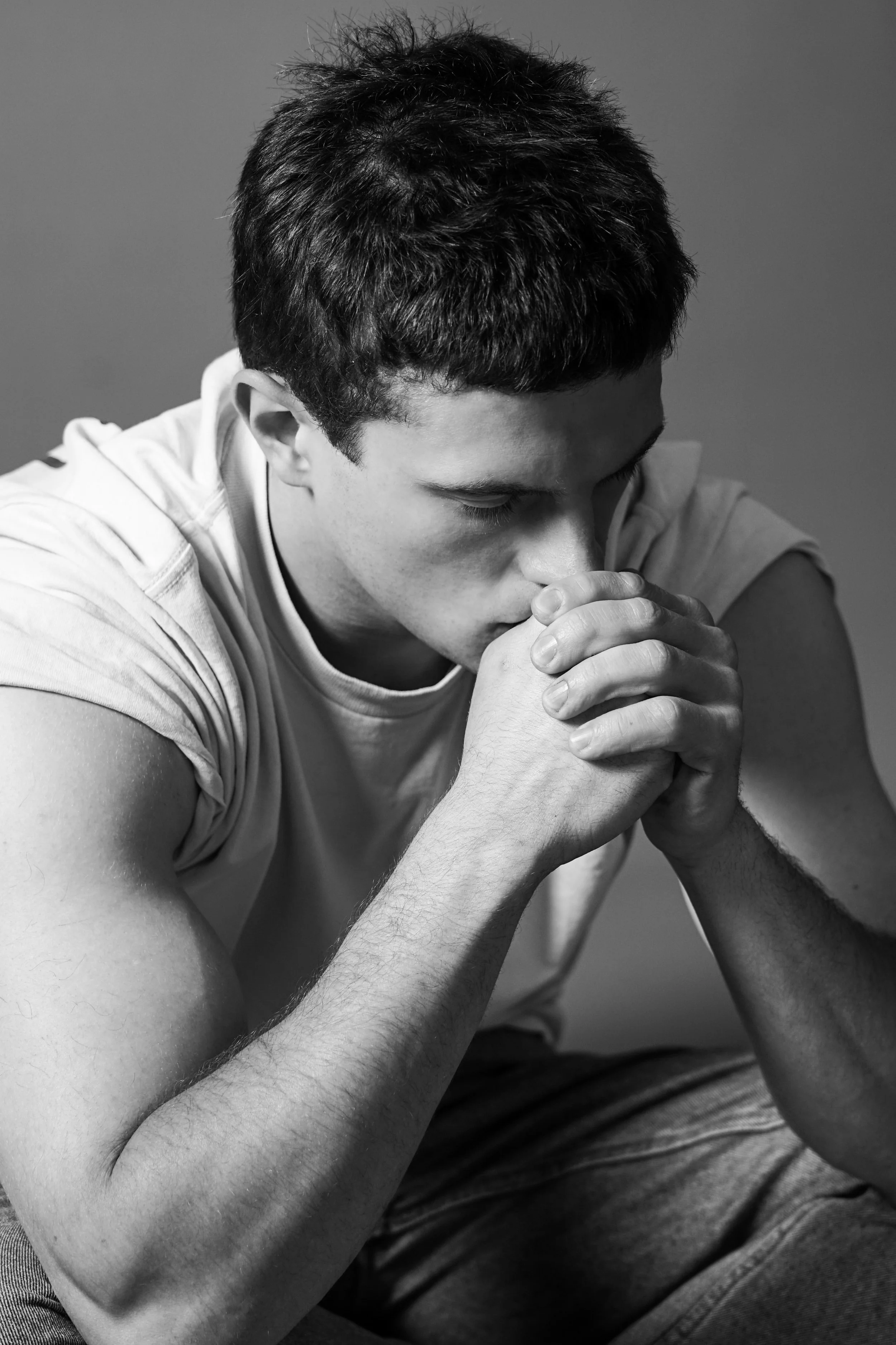 Ragazzo in contemplazione con le mani unite, testa chinata, in un'immagine in bianco e nero.