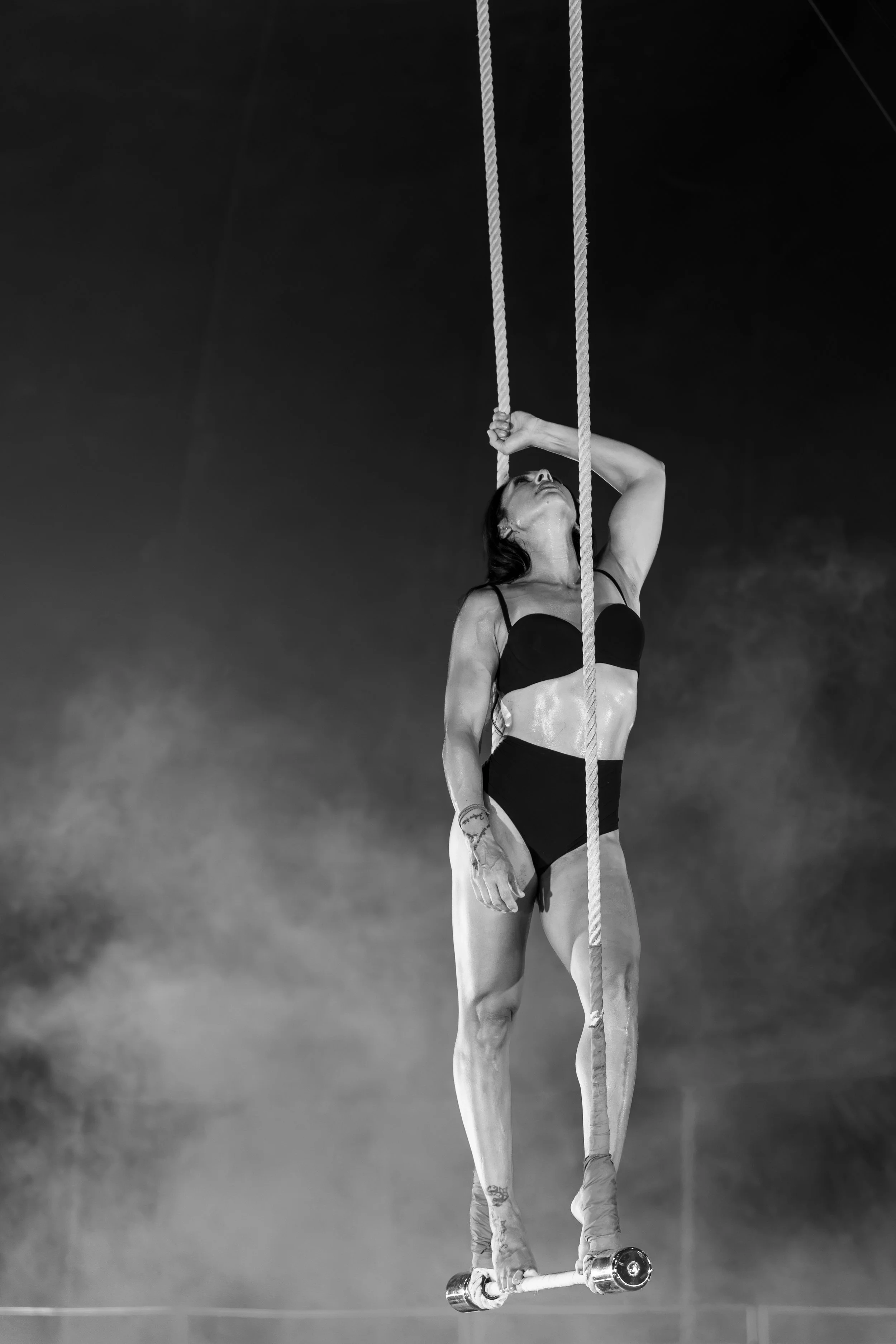 Una donna in costume da bagno si arrampica su una corda mentre si trova su un monopattino. L'immagine è in bianco e nero.