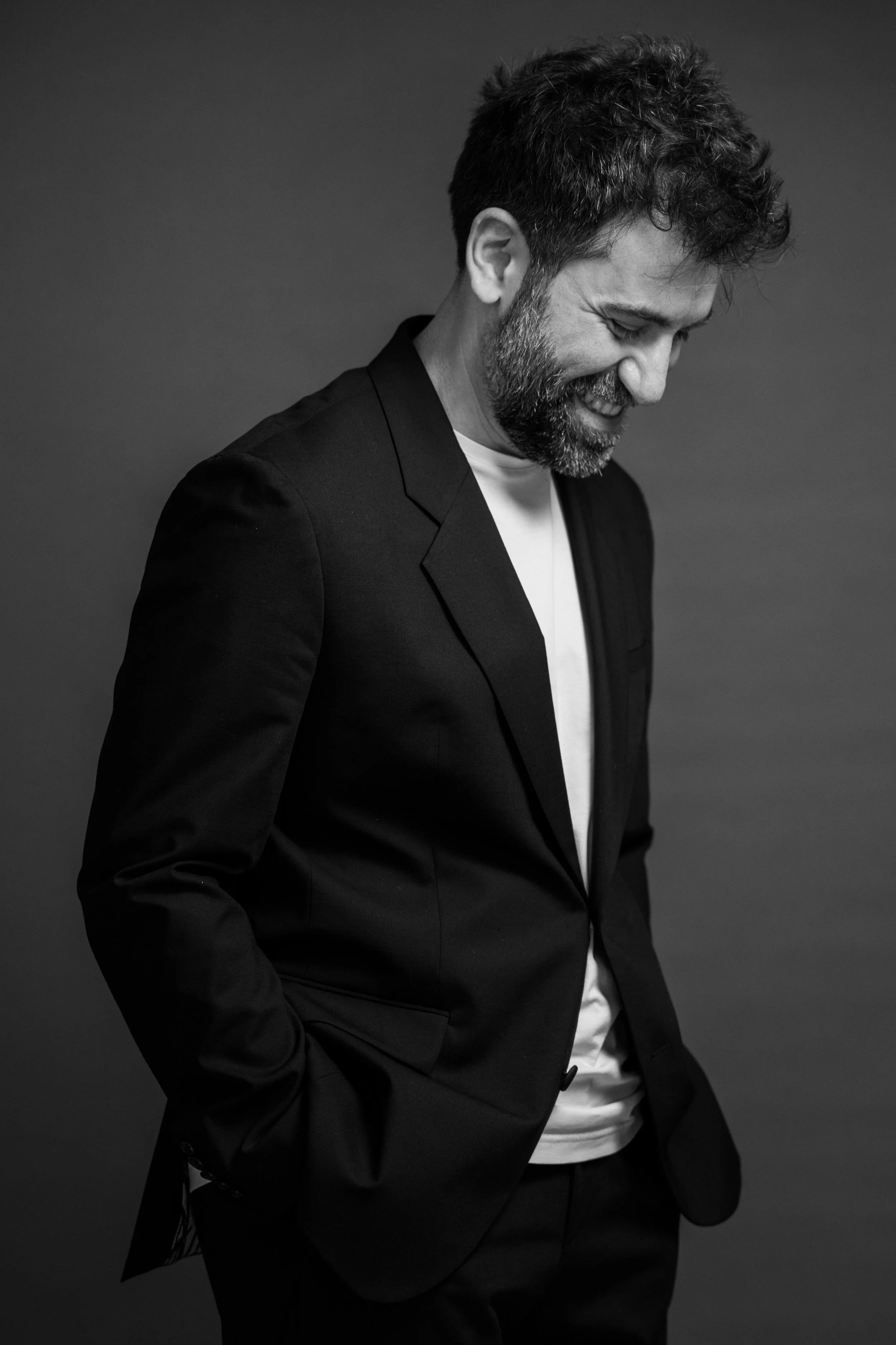 Uomo con barba e capelli ricci, vestito di nero, che sorride con gli occhi chiusi, in un'immagine in bianco e nero.