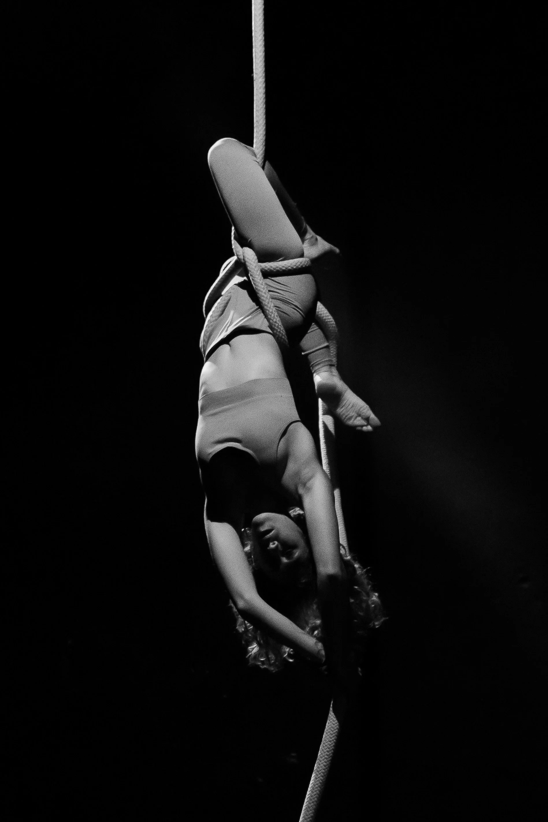 Una donna si esibisce su un'asta di trapezio in un'illuminazione drammatica, in posa acrobatica.