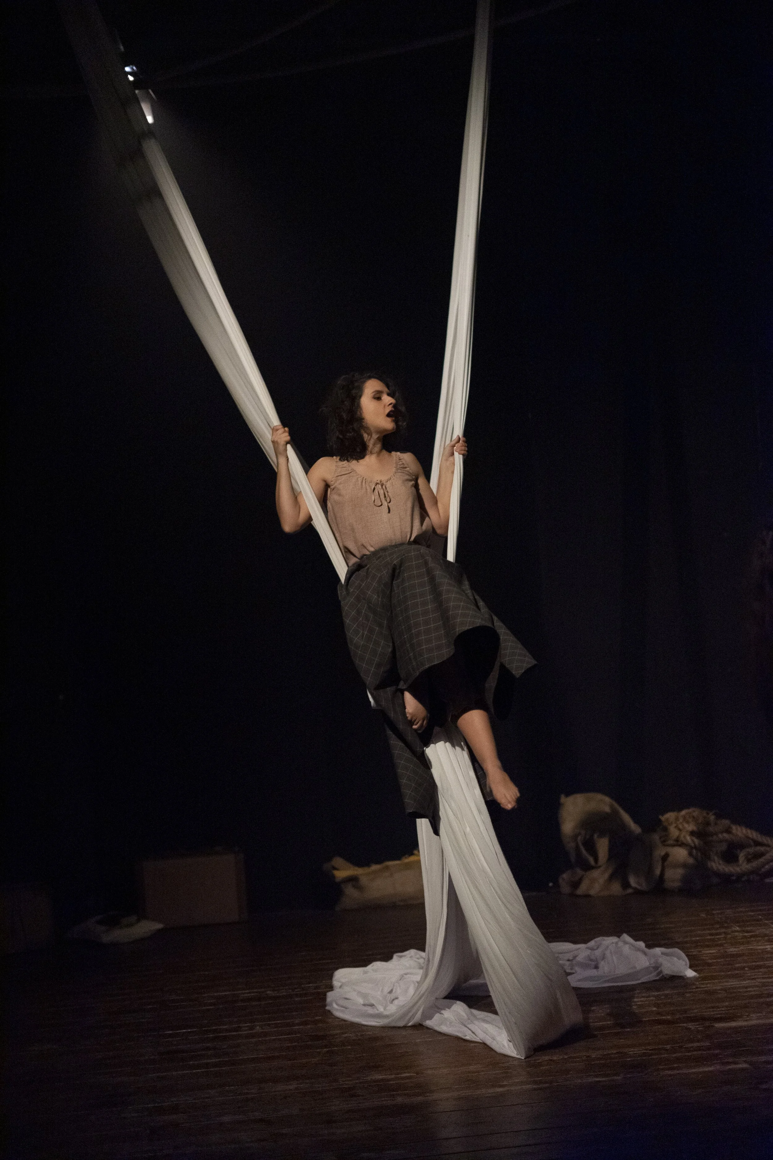 Performance teatrale con una donna che si siede su un'asse di stoffa sospesa, vestita con abiti casual, sul palcoscenico di uno spettacolo teatrale.