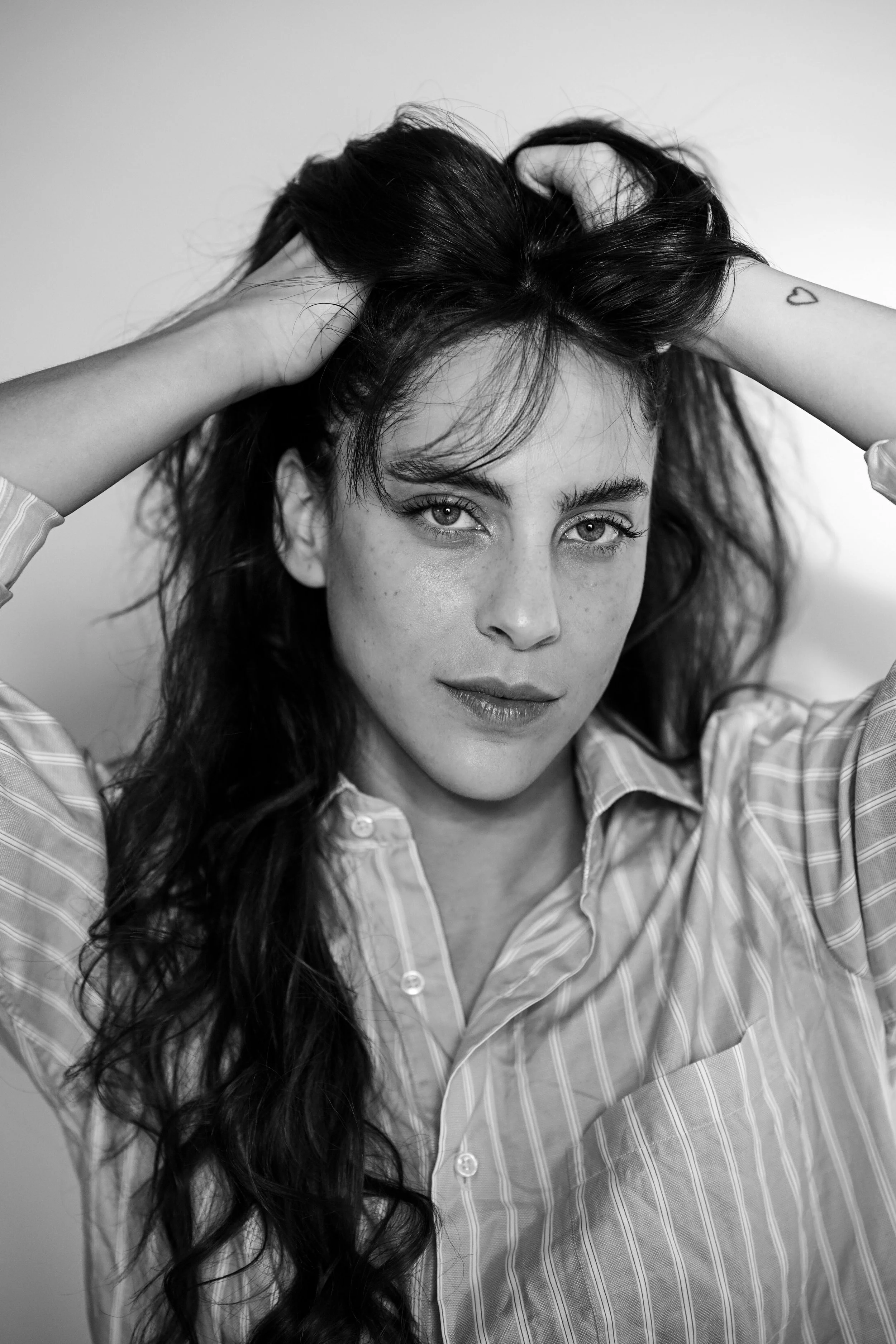 Ragazza con capelli lunghi, scura, che si sistema i capelli con le mani, indossa una camicia a righe.