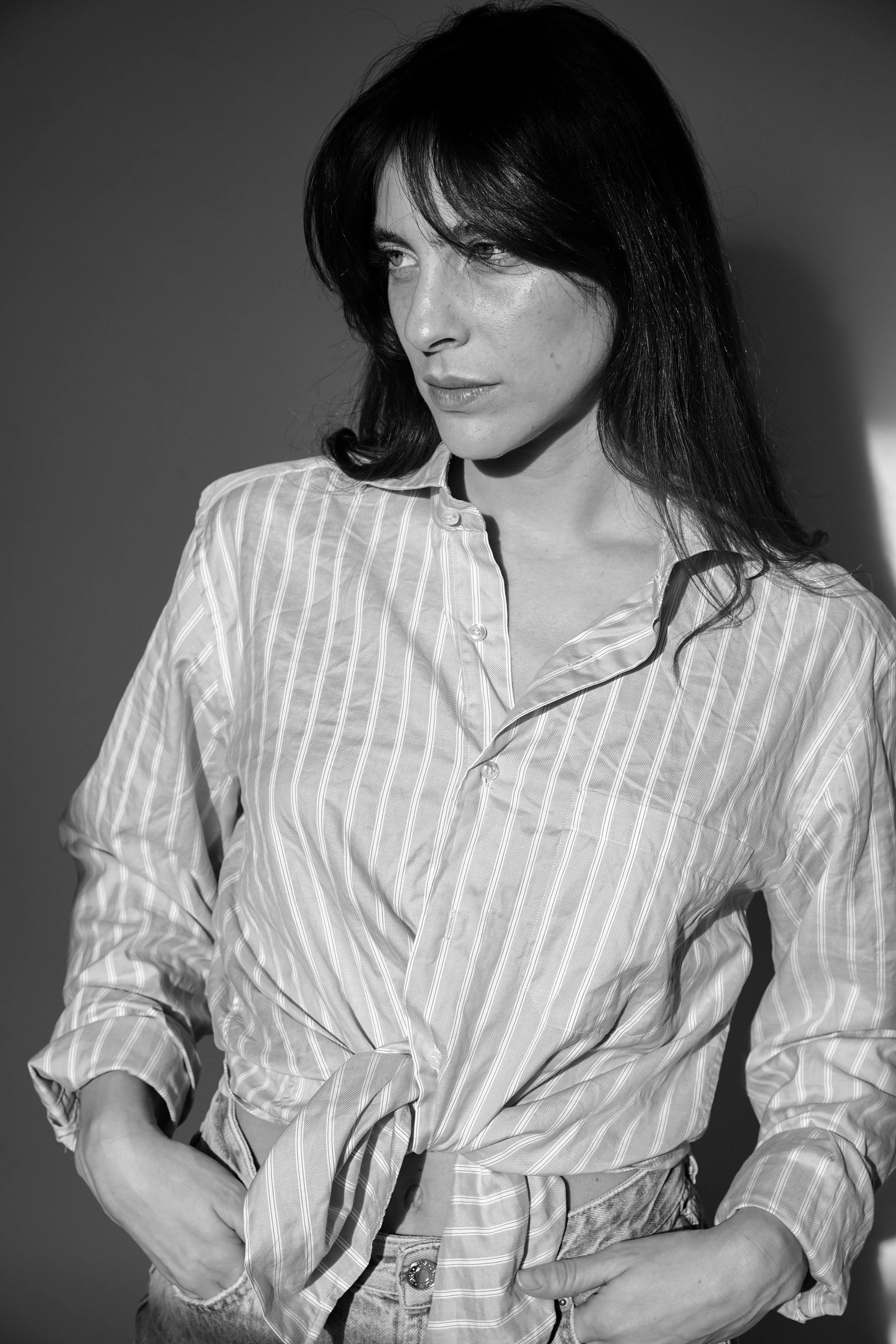 Ragazza con camicia a righe e pantaloni in denim, che guarda a destra, in bianco e nero.