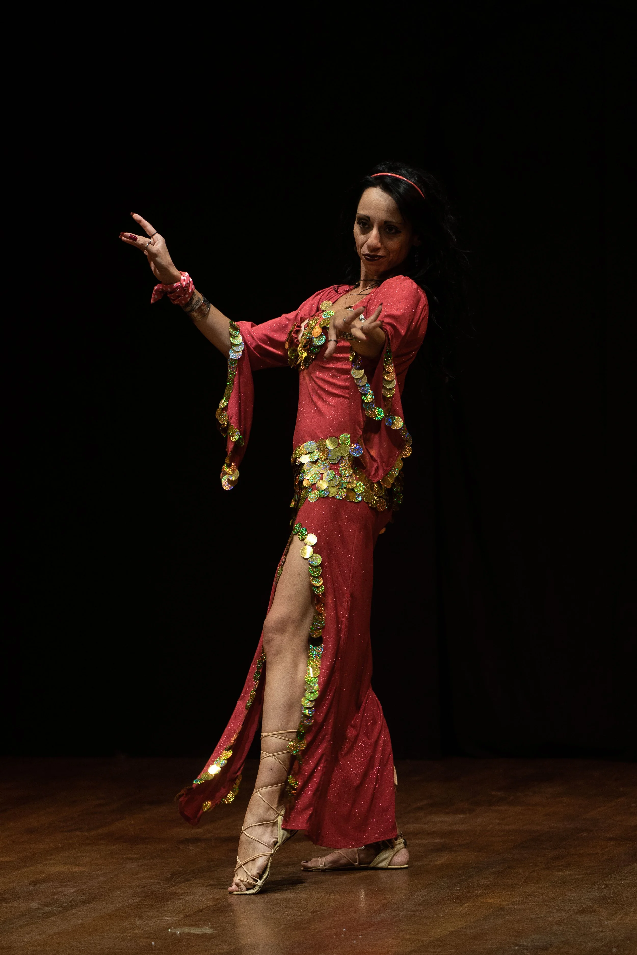 Donna che danza in abito rosso decorato con paillettes e riferimenti di salsa, con anche scarpe da ballo, in un palco con sfondo nero.