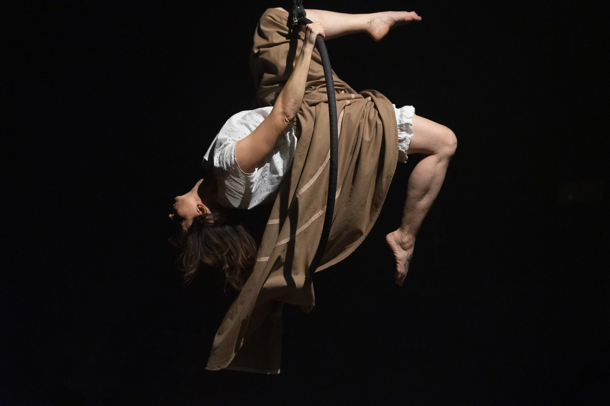 Performance di danza con due persone che si intrecciano, una in posizione capovolta e l'altra a sostegno, in un ambiente con sfondo scuro.