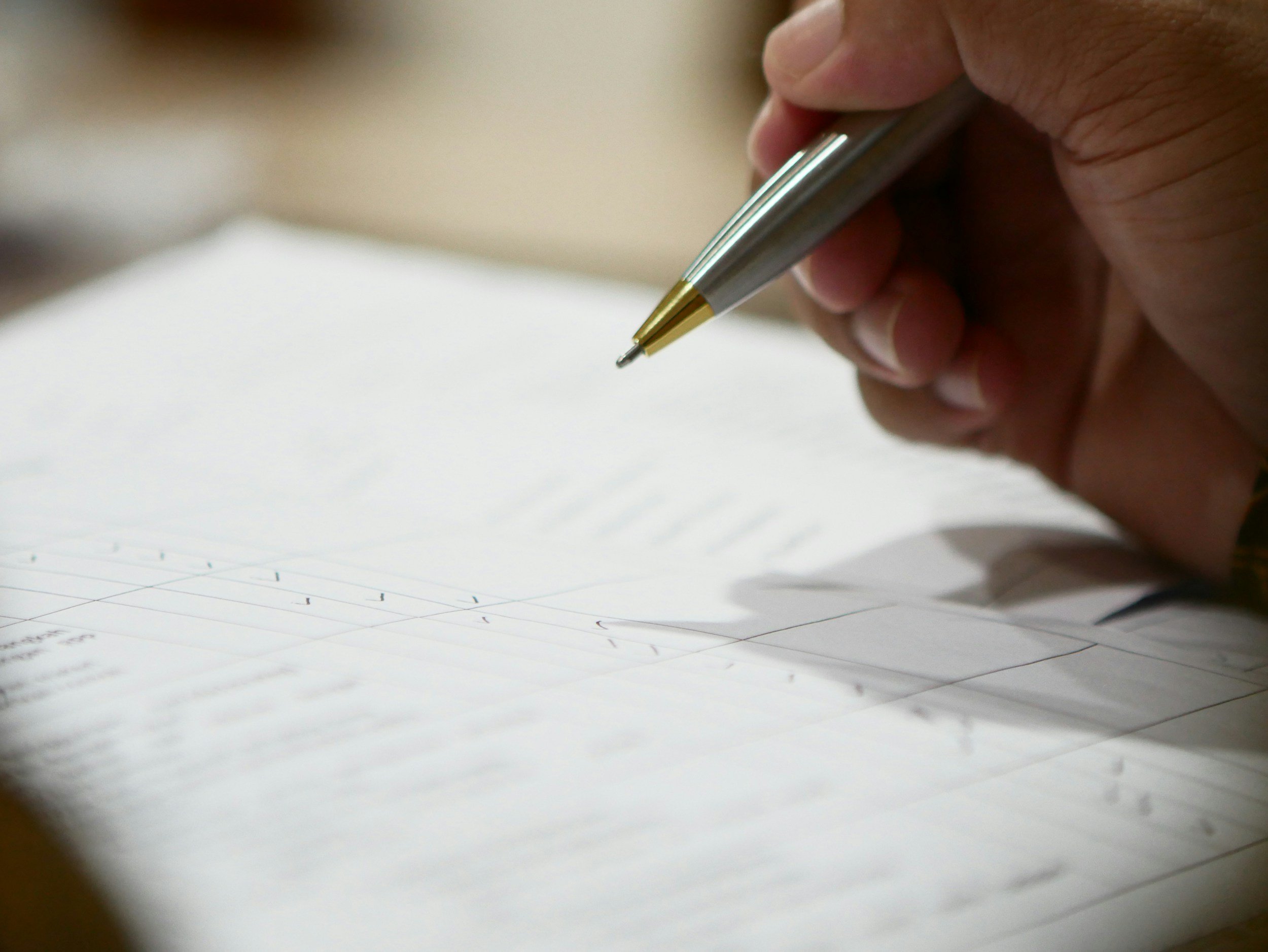 Close-up of a person's hand holding a silver and gold pen writing on lined paper.
