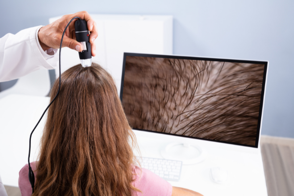Doctor Trichologist examining a patient's scalp with a dermatoscope in an office setting.