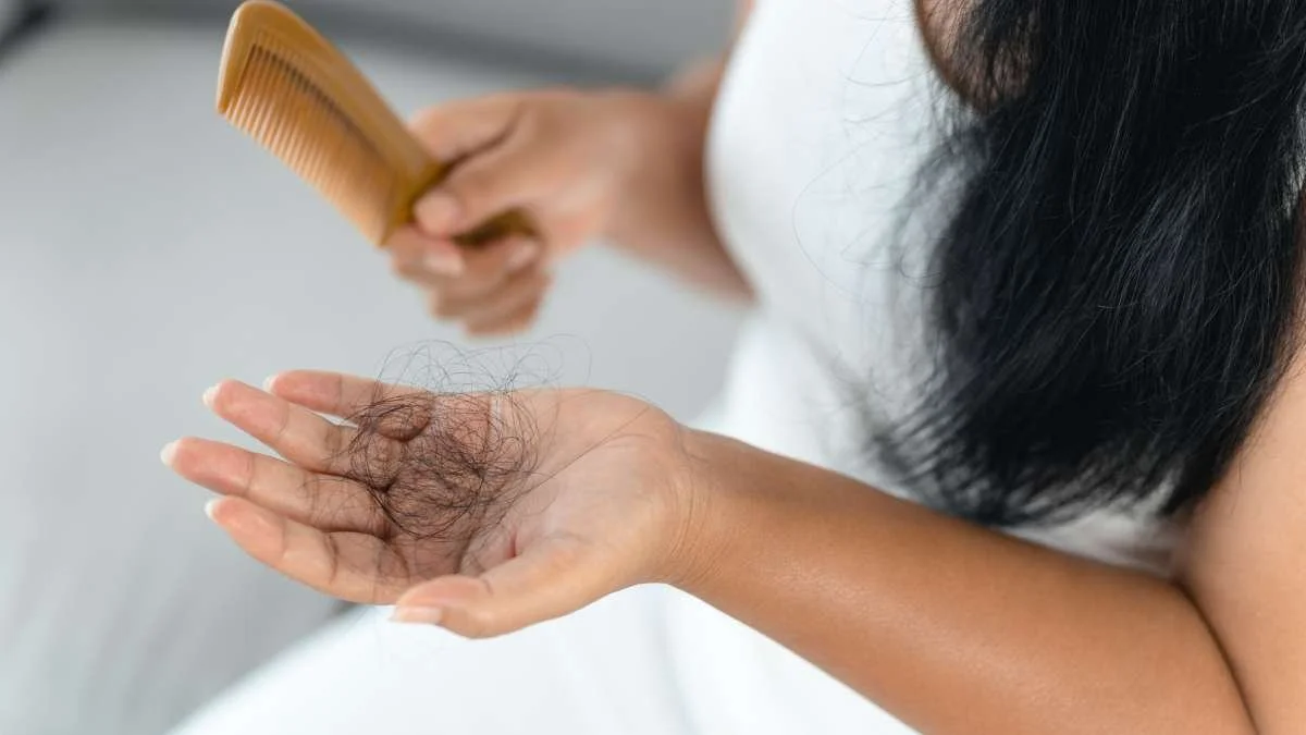 A woman with long black hair is holding a small pile of gray hair in her hand, while using a yellow comb to remove hair from her head. Suffers from hair loss