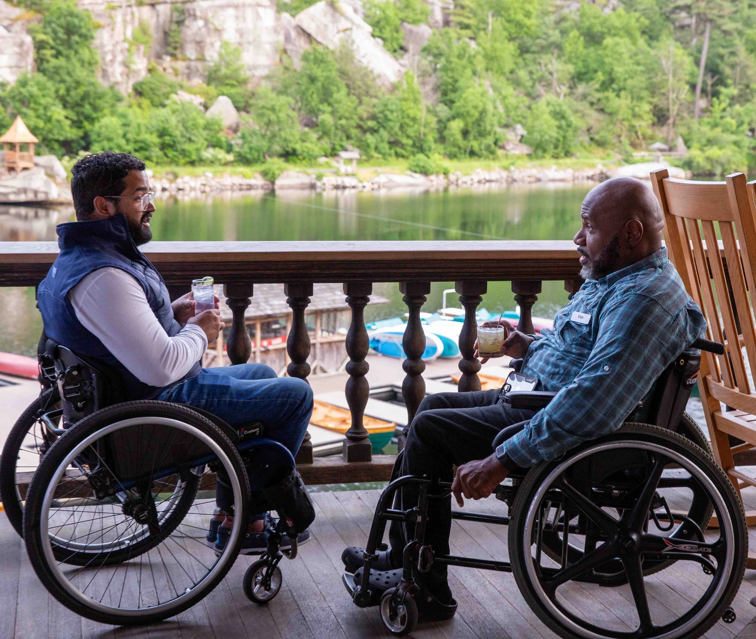 Two men in wheelchairs speaking with each other in front of a lake setting