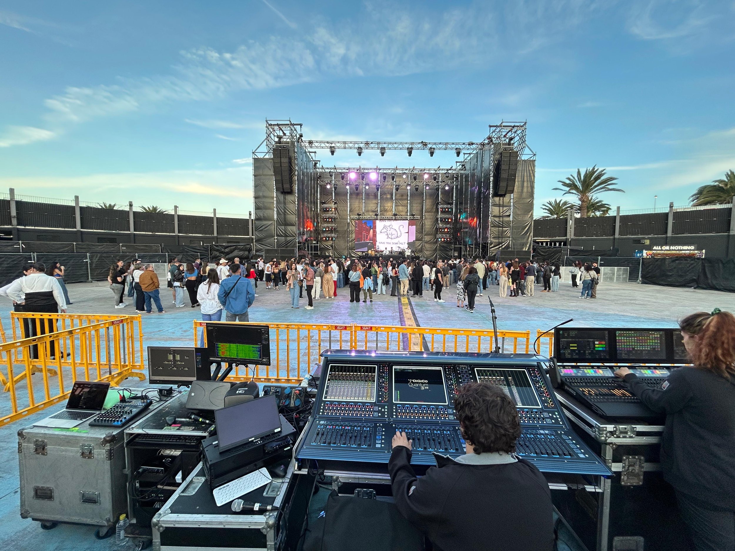 Técnico de sonido operando mezcla FOH durante festival de música con escenario principal y público en directo