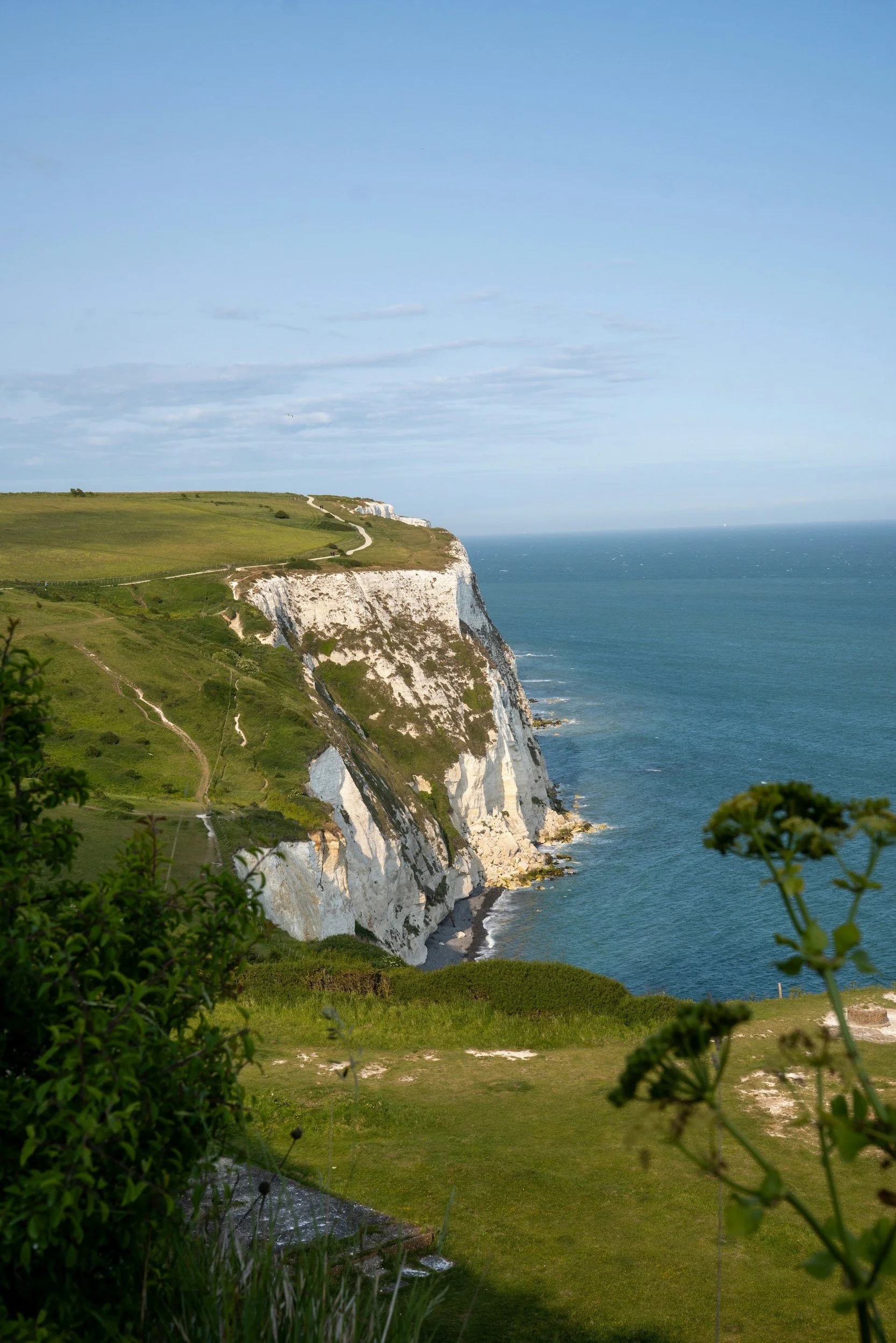 Cliffs overlooking the ocean with grassy paths leading to the top, under a partly cloudy sky.