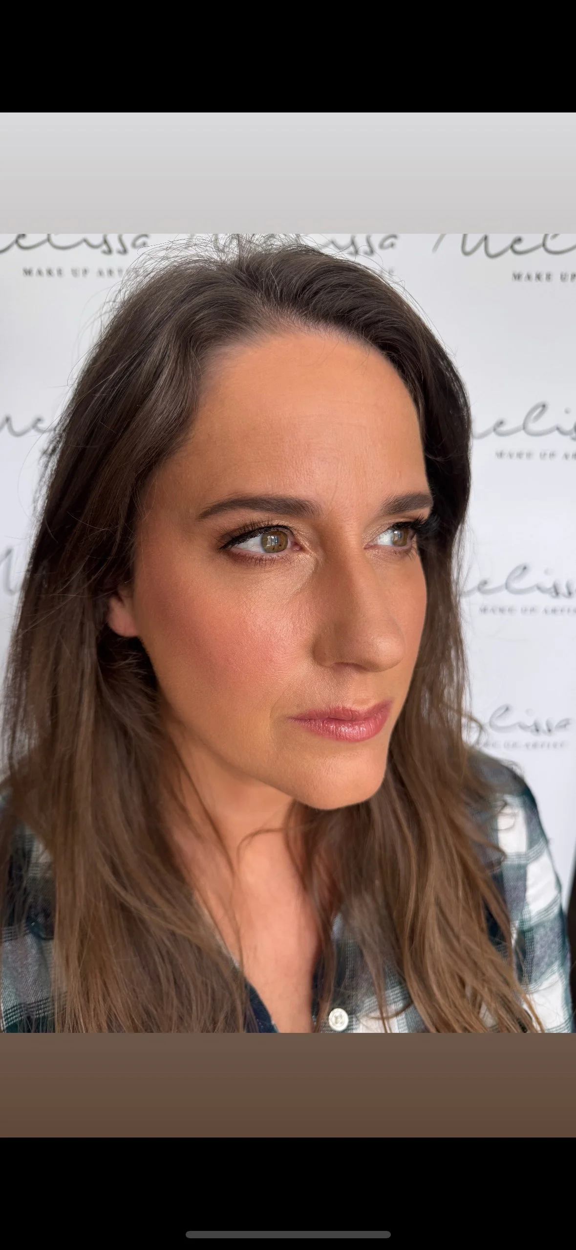 A woman with long brown hair and light skin looking slightly to the side, with a blurred background featuring written text.