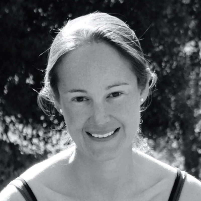 Black and white photo of a smiling woman with short hair outdoors, blurred trees in the background.