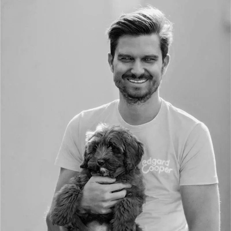 Smiling man holding a fluffy puppy, wearing a t-shirt, in black and white.