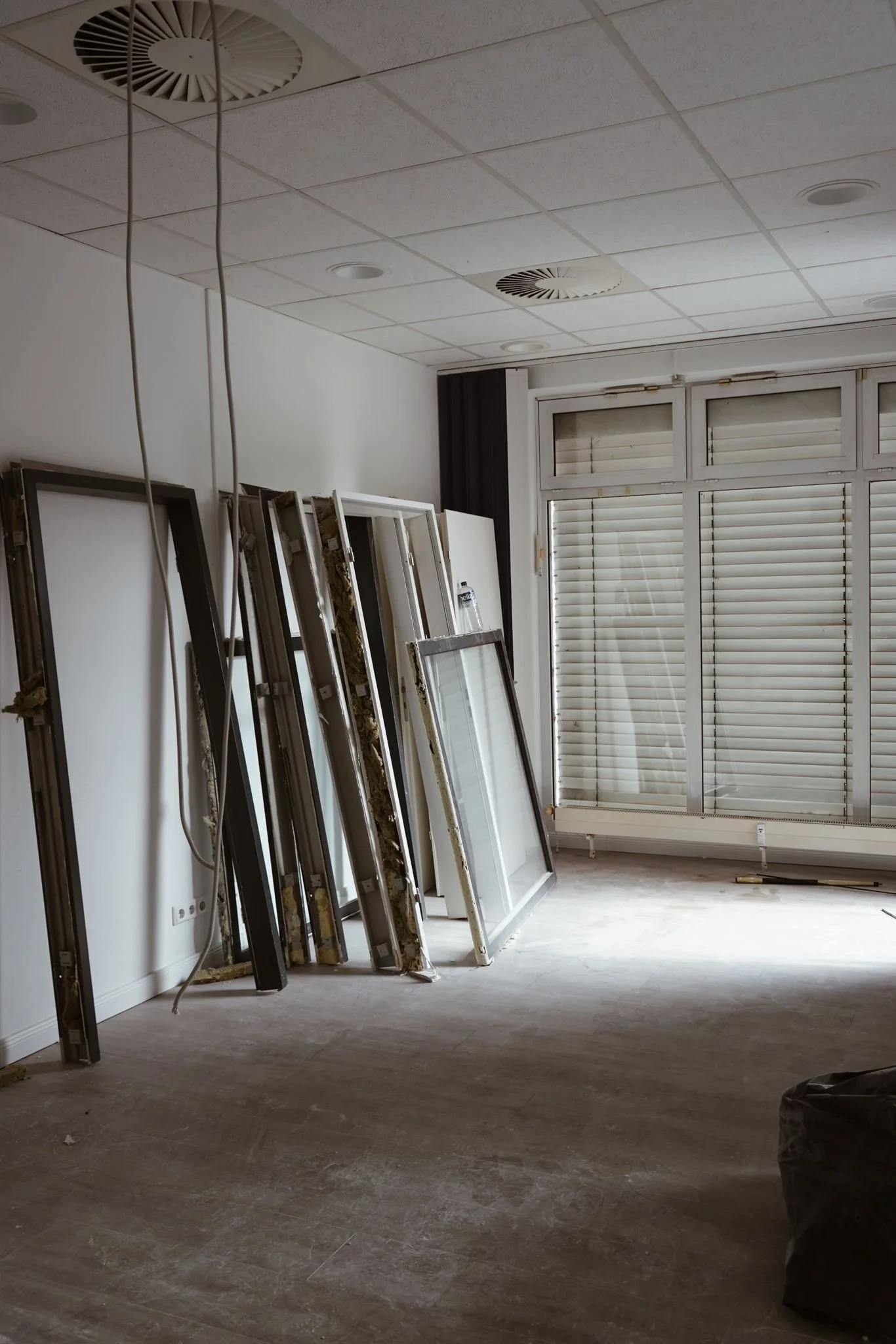 Leeres Zimmer mit Fensterläden und gestapelten Fensterramen, vermutlich bei Renovierungsarbeiten.