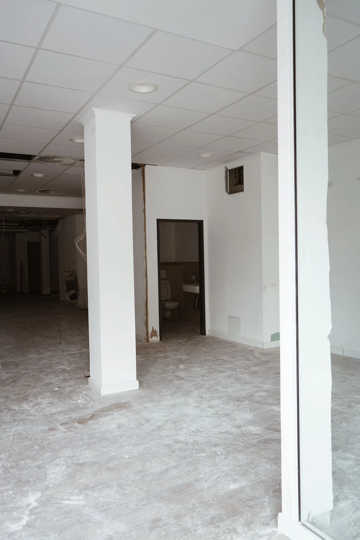 Innenraum eines Gebäudes unter Renovierung, mit weißen Wänden, einem weißen Sink im Badezimmer, und einem offenen Raum, der gerade renoviert wird.