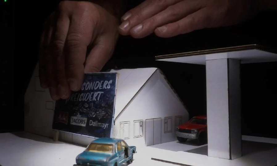 A scene takes place at a miniature gas station. The camera then turns to the provincial road on the right (AR)..