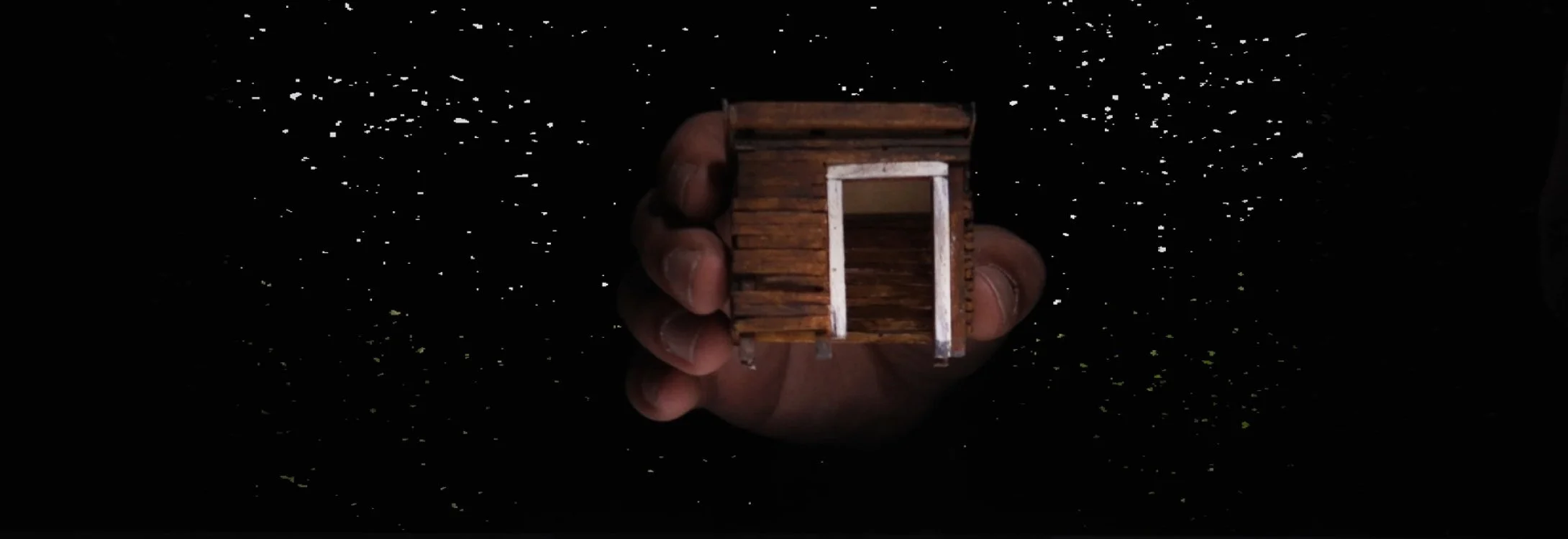 From digital noise (AR), the hand of a performer begins to build a miniature world, house by house.