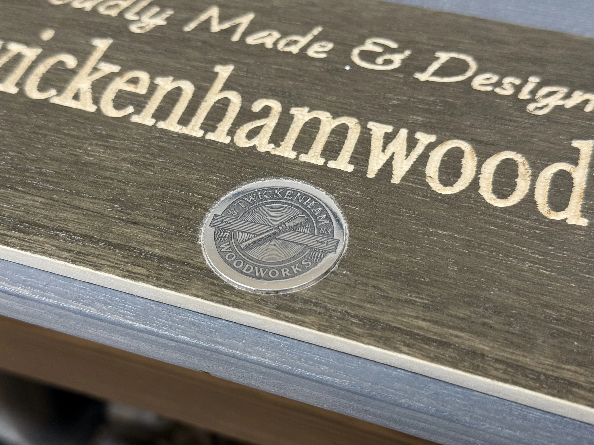Close-up of engraved wooden sign with metal logo at the bottom that reads 'Wickenden Woodworks' and emphasizes the handmade and crafted quality.