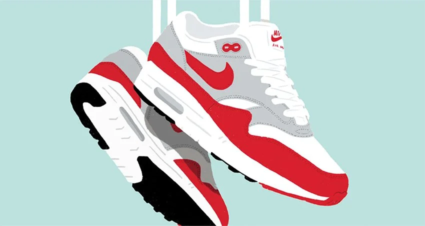 A pair of Nike Air Max sneakers, white, red, gray, and black, hanging from a white shoe rack