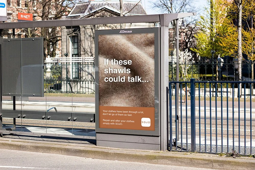 Bus stop advertisement promoting repair and alteration of clothes with SOJO, featuring a close-up of a brown fabric shawl.