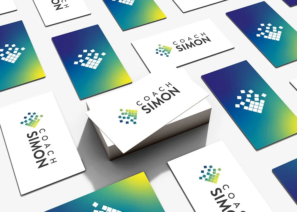 Business cards with a colorful logo and the name 'Coach Simon' arranged on a white surface.