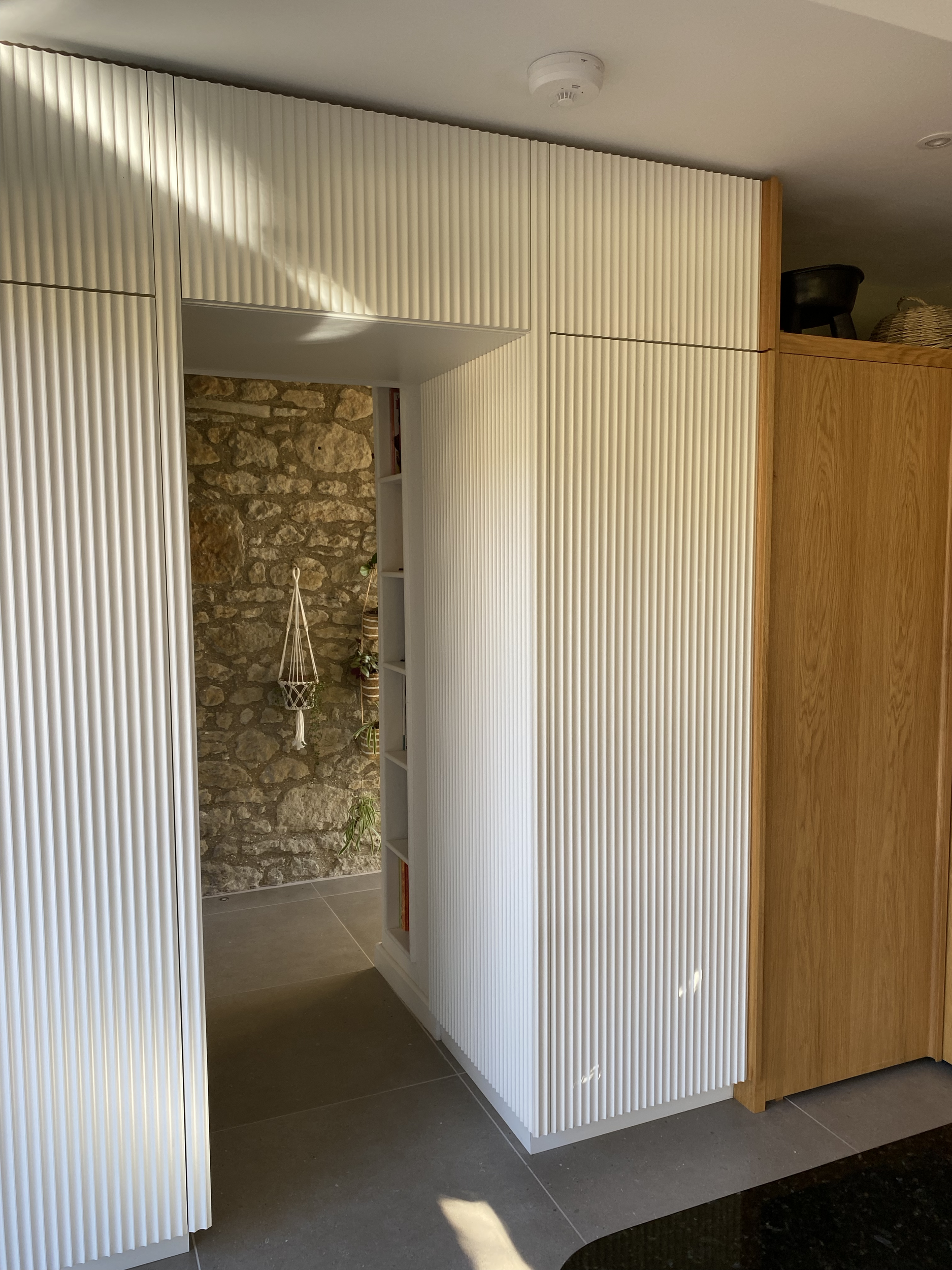 White vertical blinds partially open, revealing a small outdoor area with a stone wall and some plants.