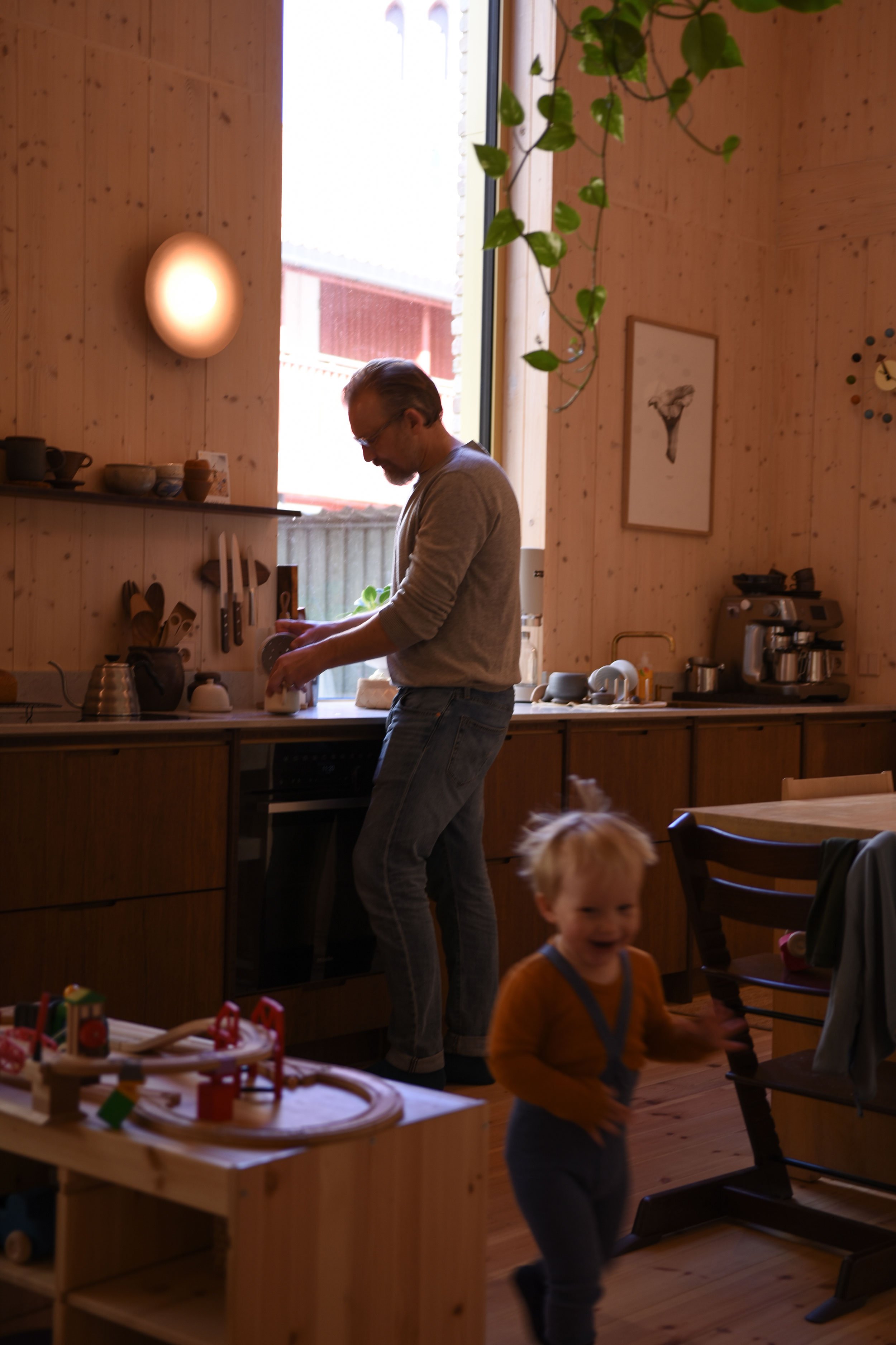 Mann lager kaffi på kjøkkenet med mørke valnøtt fronter og høyt vindu bak.