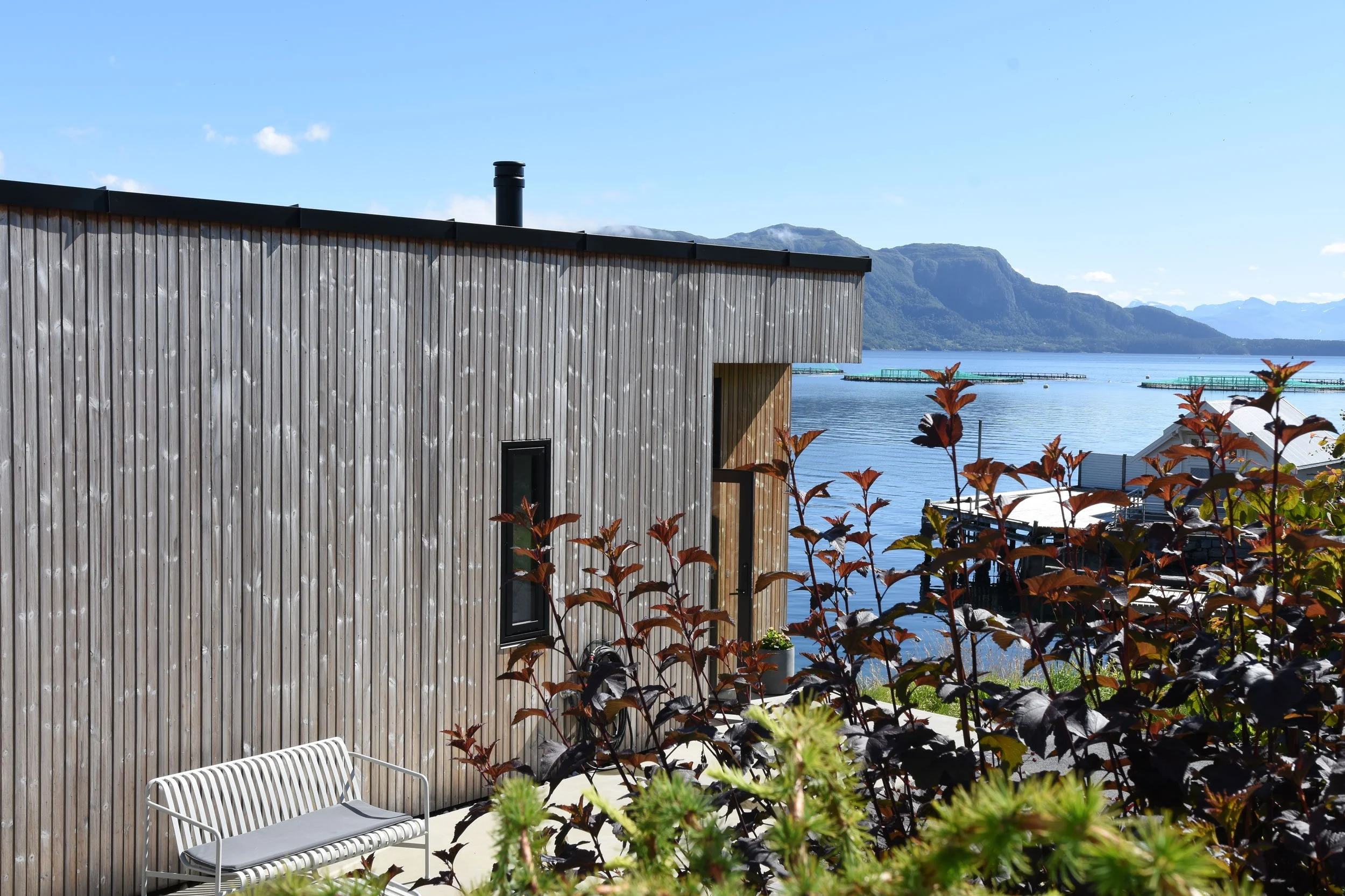 Atrium med hage på en varm og solfylt sommerdag med utsikt til fjell og sjø.