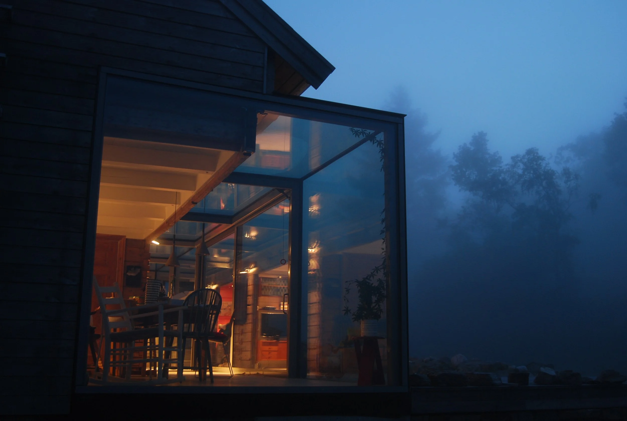 Gamlehuset med glasstilbygget som en kontrast til den klassiske husformen. Kveld med tåke i skogen utenfor.