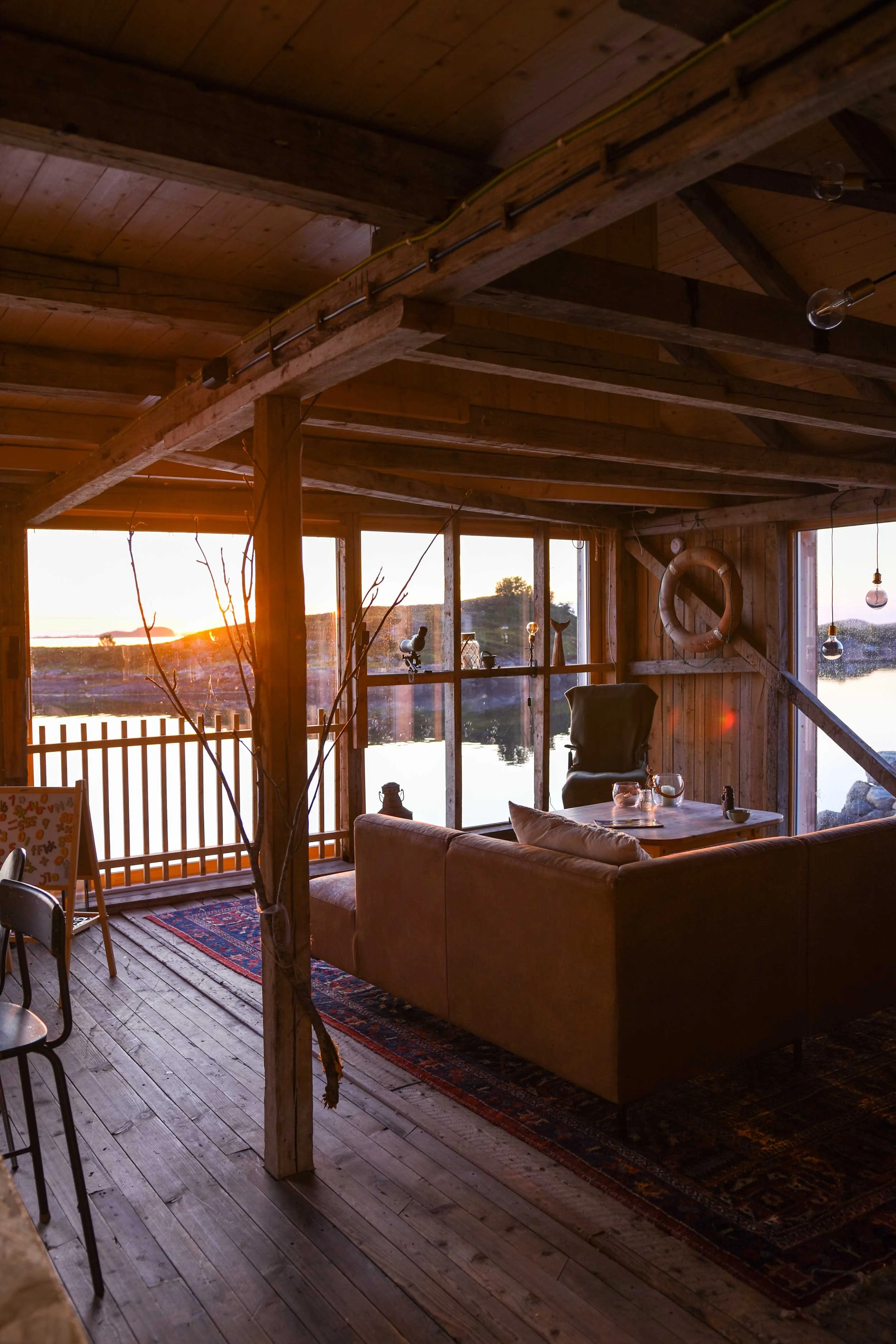 Skinnsofa med utsikt over havet og solnedgangen. Rustikk interiør med bevart konstruksjon i eldre sjøbu.