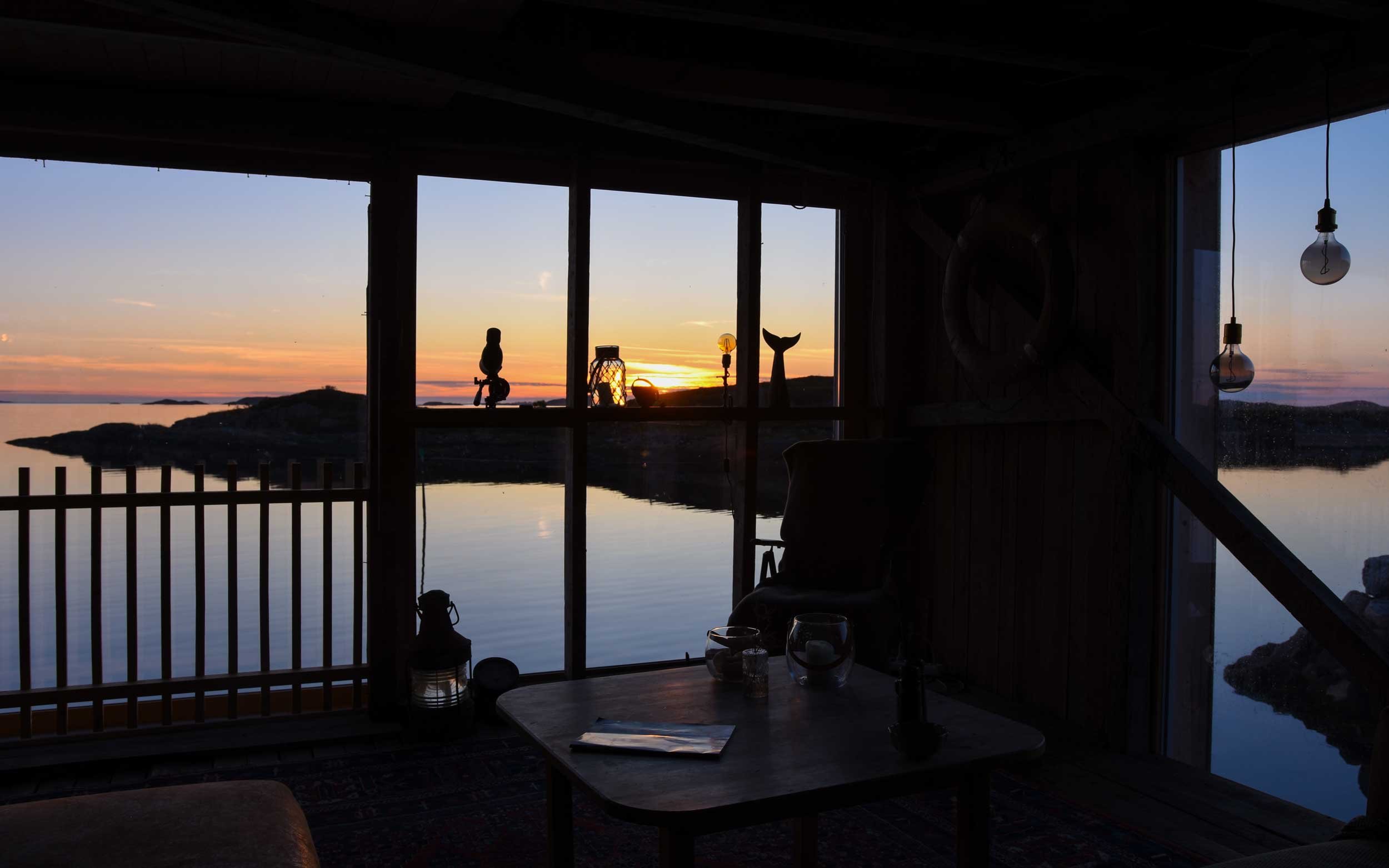 Siste solstrålene over horisonten skinner gjennom vinduene på den restaurerte ferie sjøbuen.