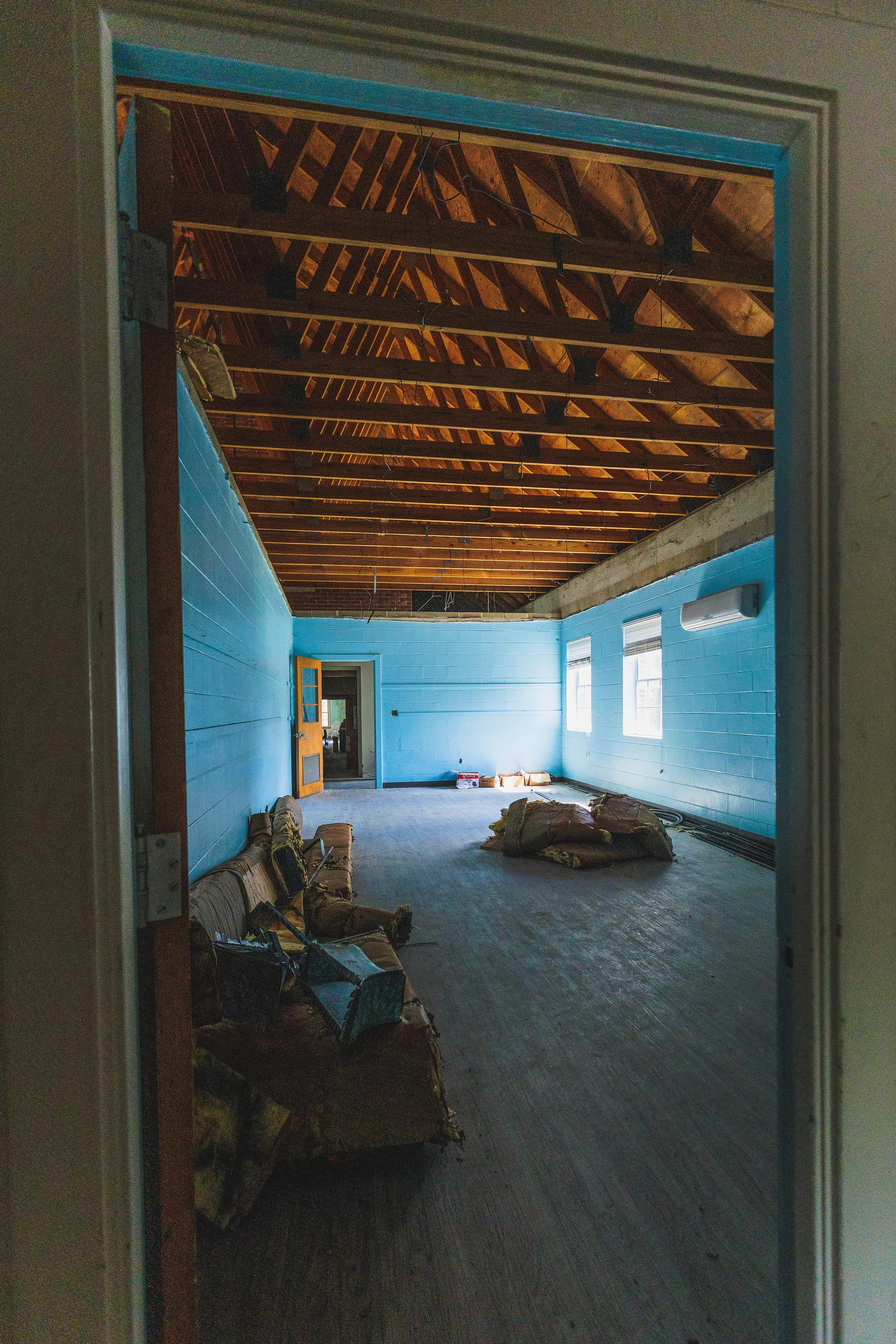 Room under renovation with blue walls, exposed ceiling beams, and construction materials on the floor.