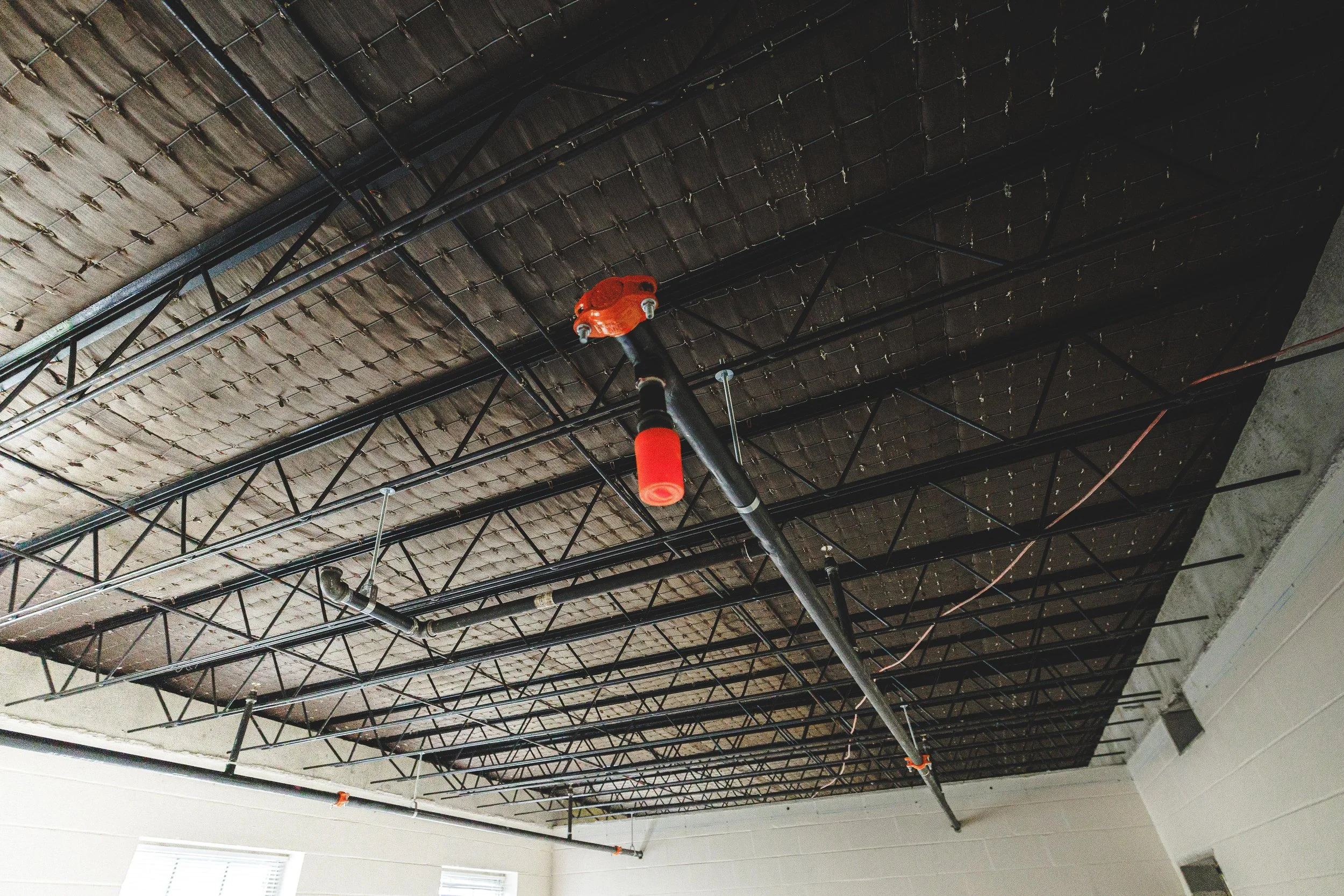 Ceiling with exposed metal framework, pipes, and red sprinkler system components in a building under construction or renovation.