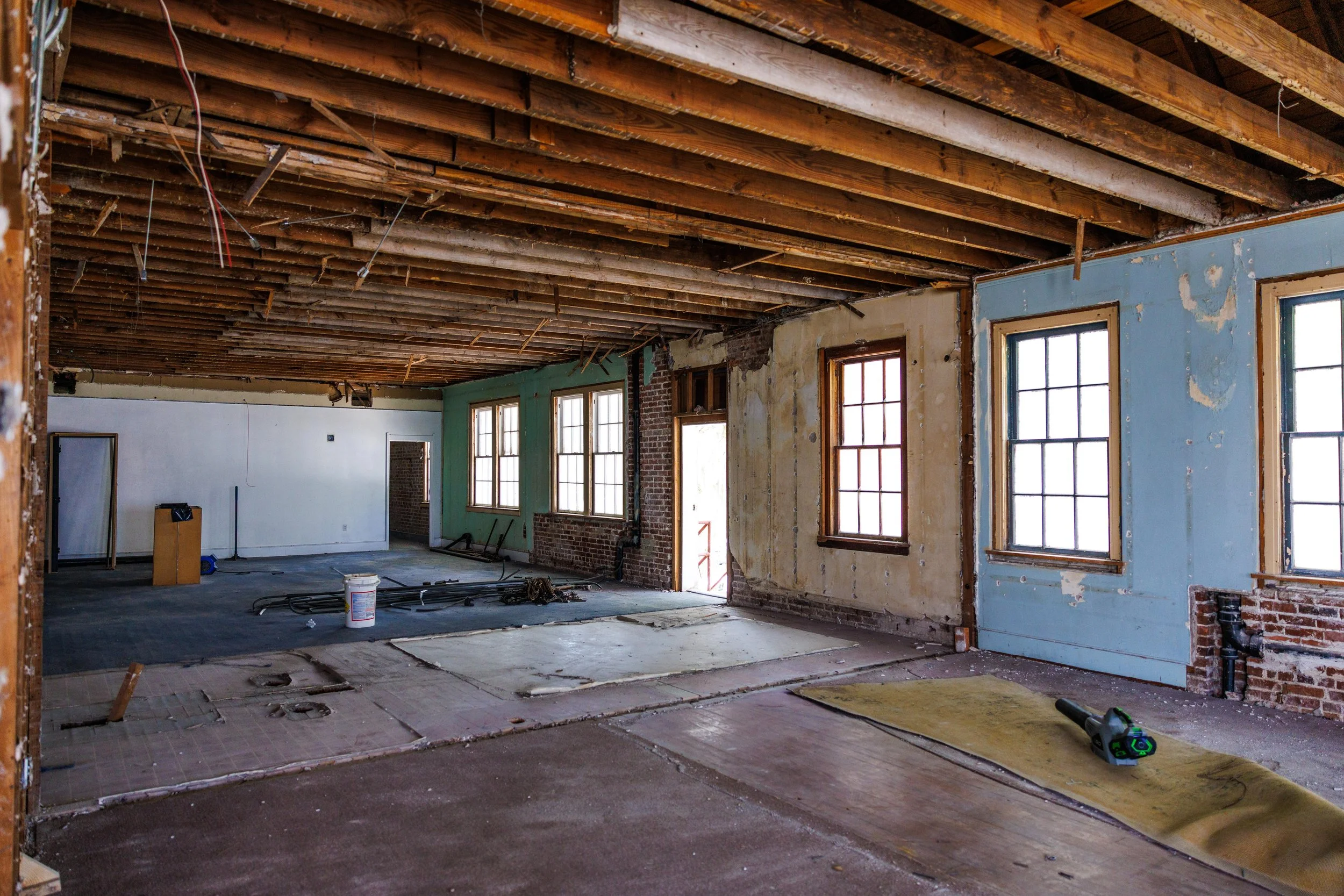 Interior of a building under renovation with exposed ceiling beams, unfinished walls, and construction tools on the floor.
