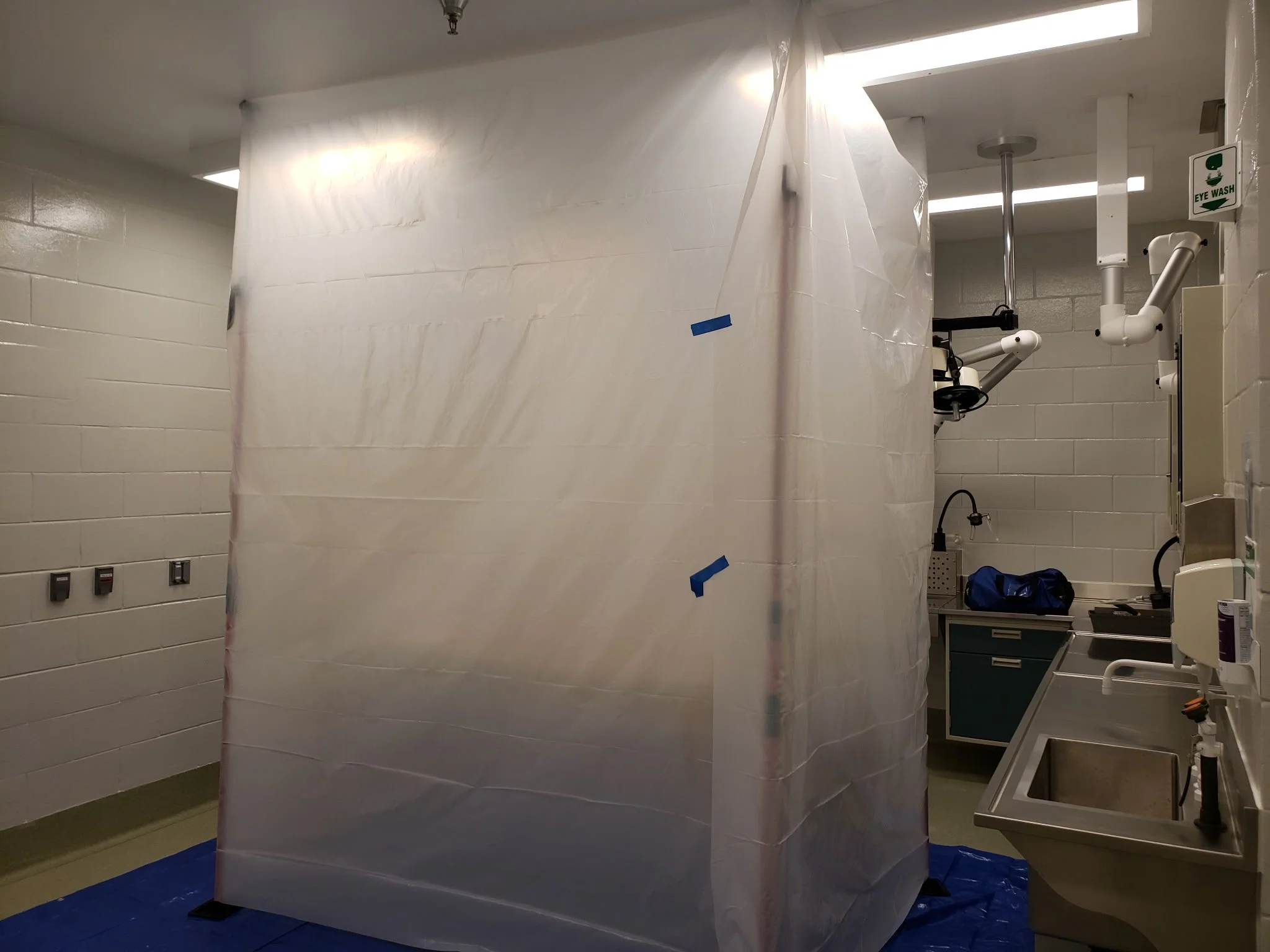Sterile medical room with plastic curtain, sink, and overhead surgical equipment, likely in a hospital or clinic.
