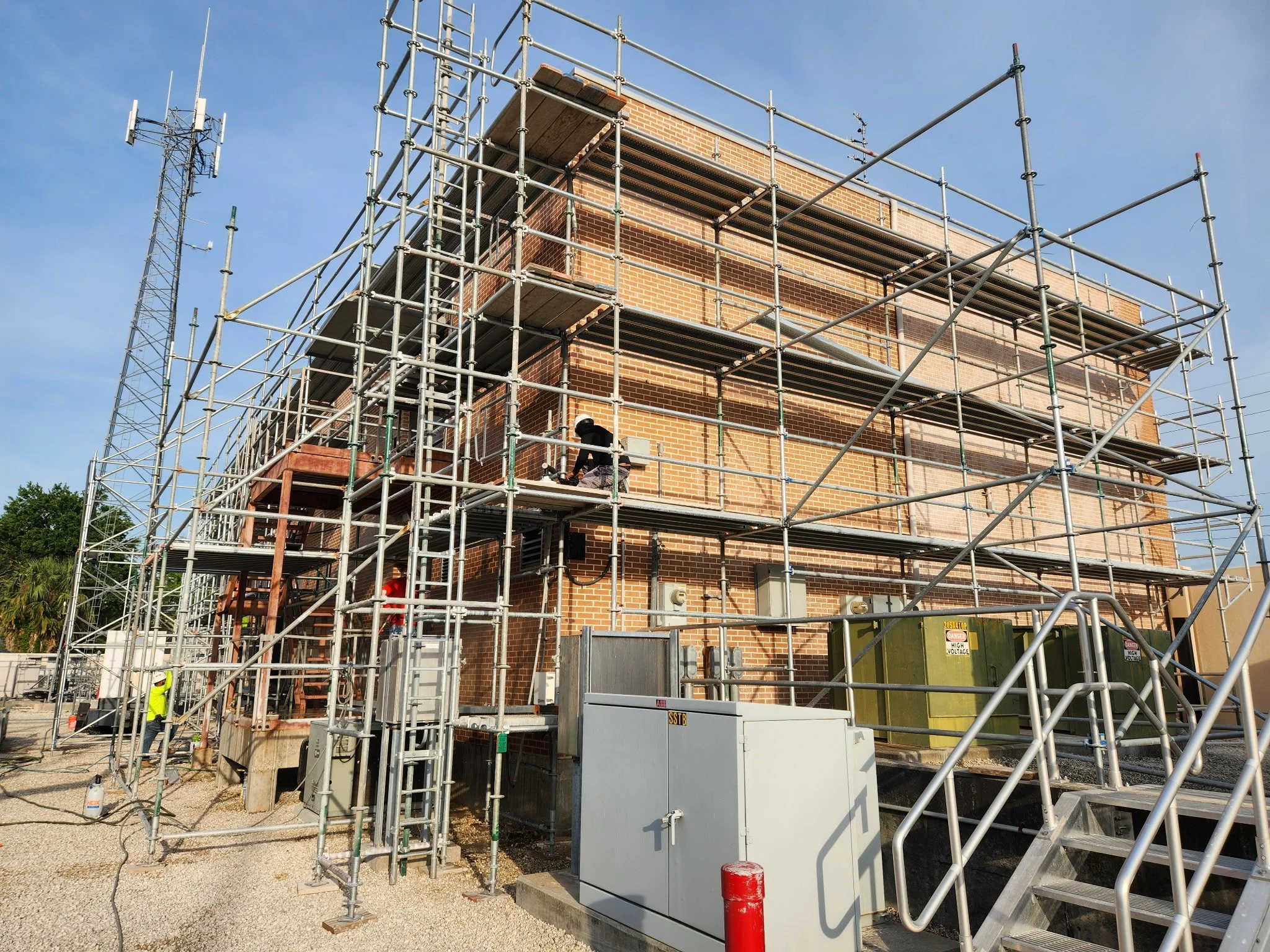 Construction workers on scaffolding working on a brick building with construction debris around.