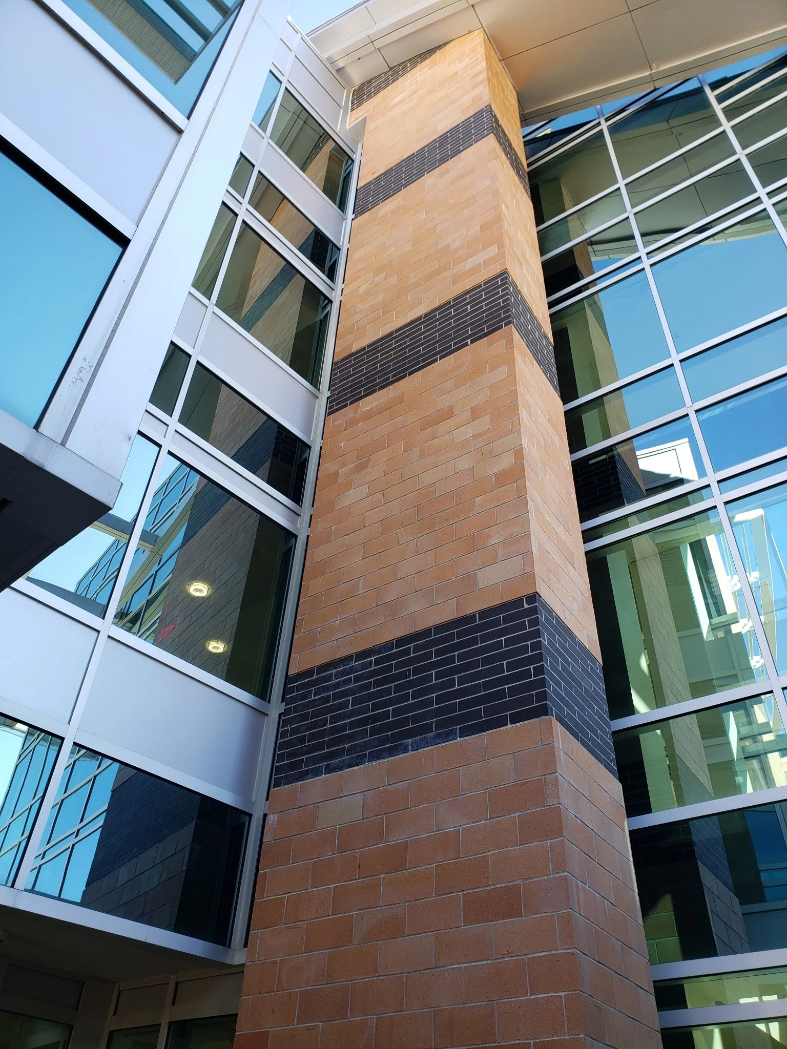 Close-up of a modern building's exterior showing brick and glass sections, with a focus on a central brick pillar featuring black brick horizontal accents.