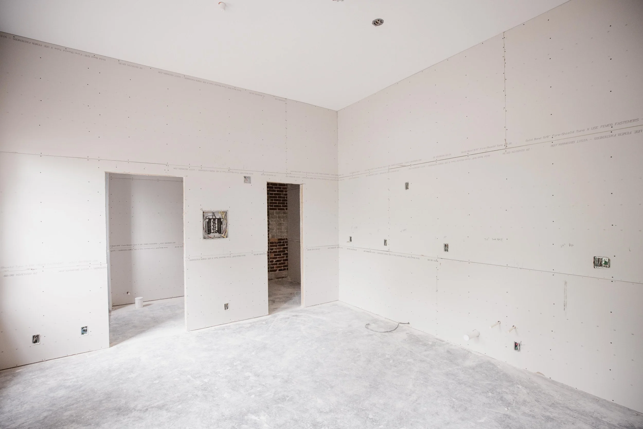 Empty room under construction with drywall installation, electrical outlets, and openings for doors and windows.